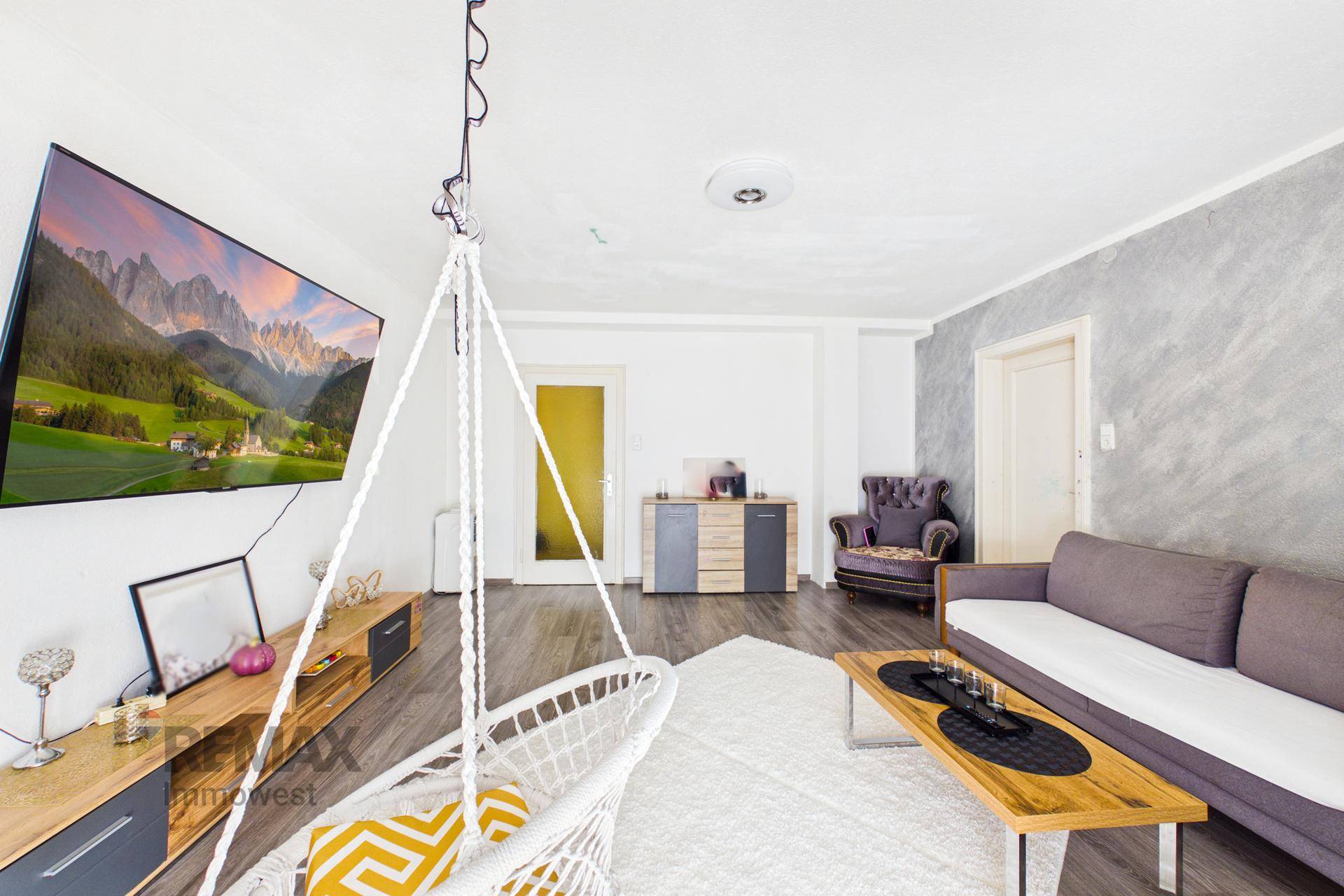 Geräumiges Wohnzimmer mit großem Fernseher, Hängesessel und Laminatboden.