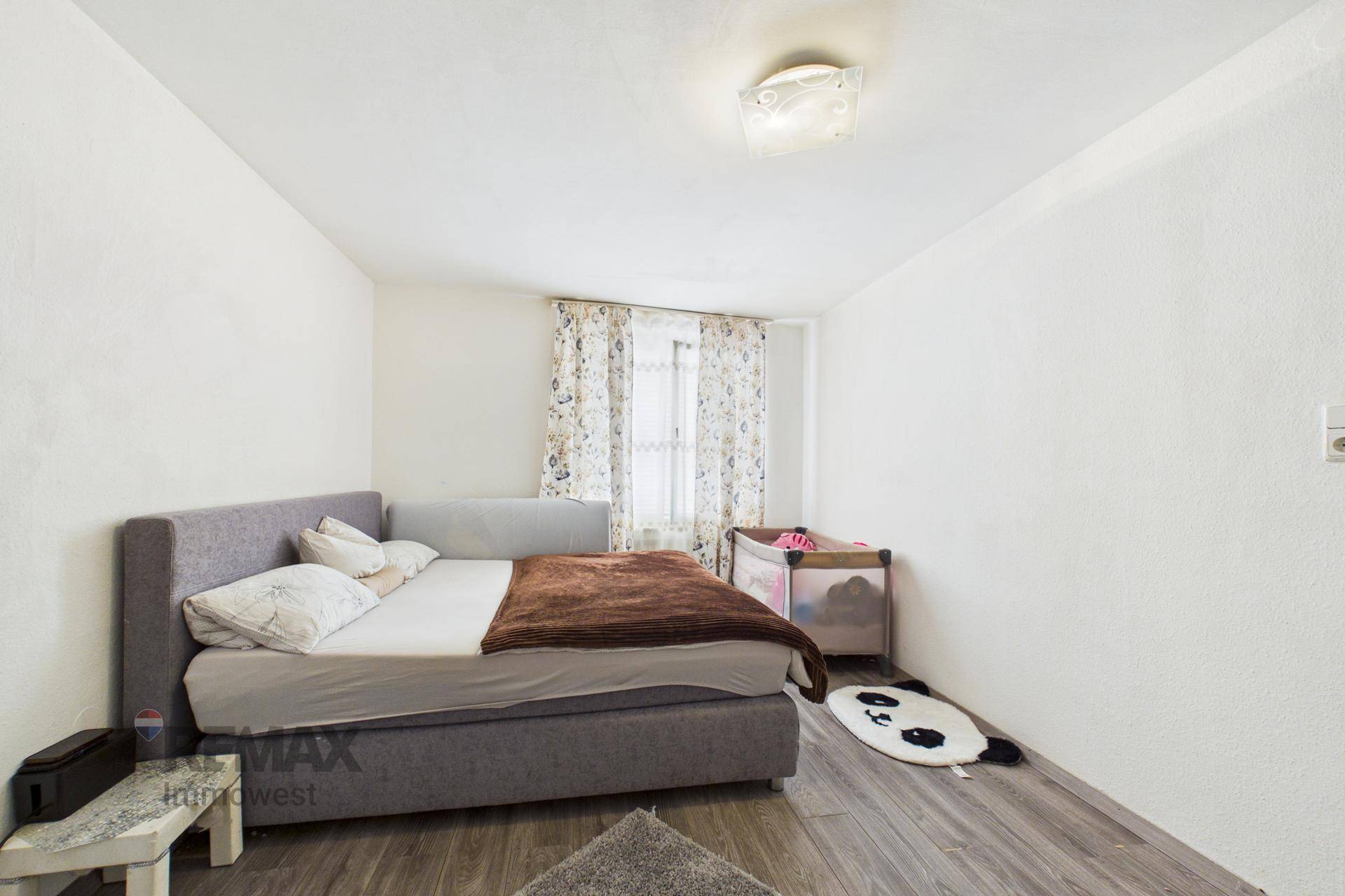 Schlafzimmer mit Doppelbett, Kinderbett und Laminatboden.