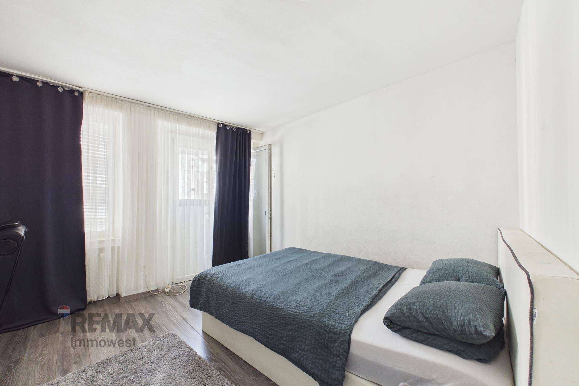 Schlafzimmer mit Doppelbett, dunklen Vorhängen und Laminatboden.
