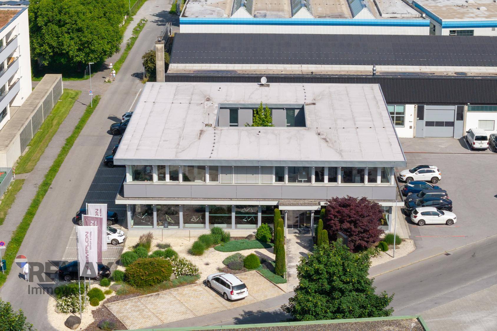Luftaufnahme eines Bürogebäudes mit Flachdach, umgeben von Parkplätzen und anderen Gewerbebauten.