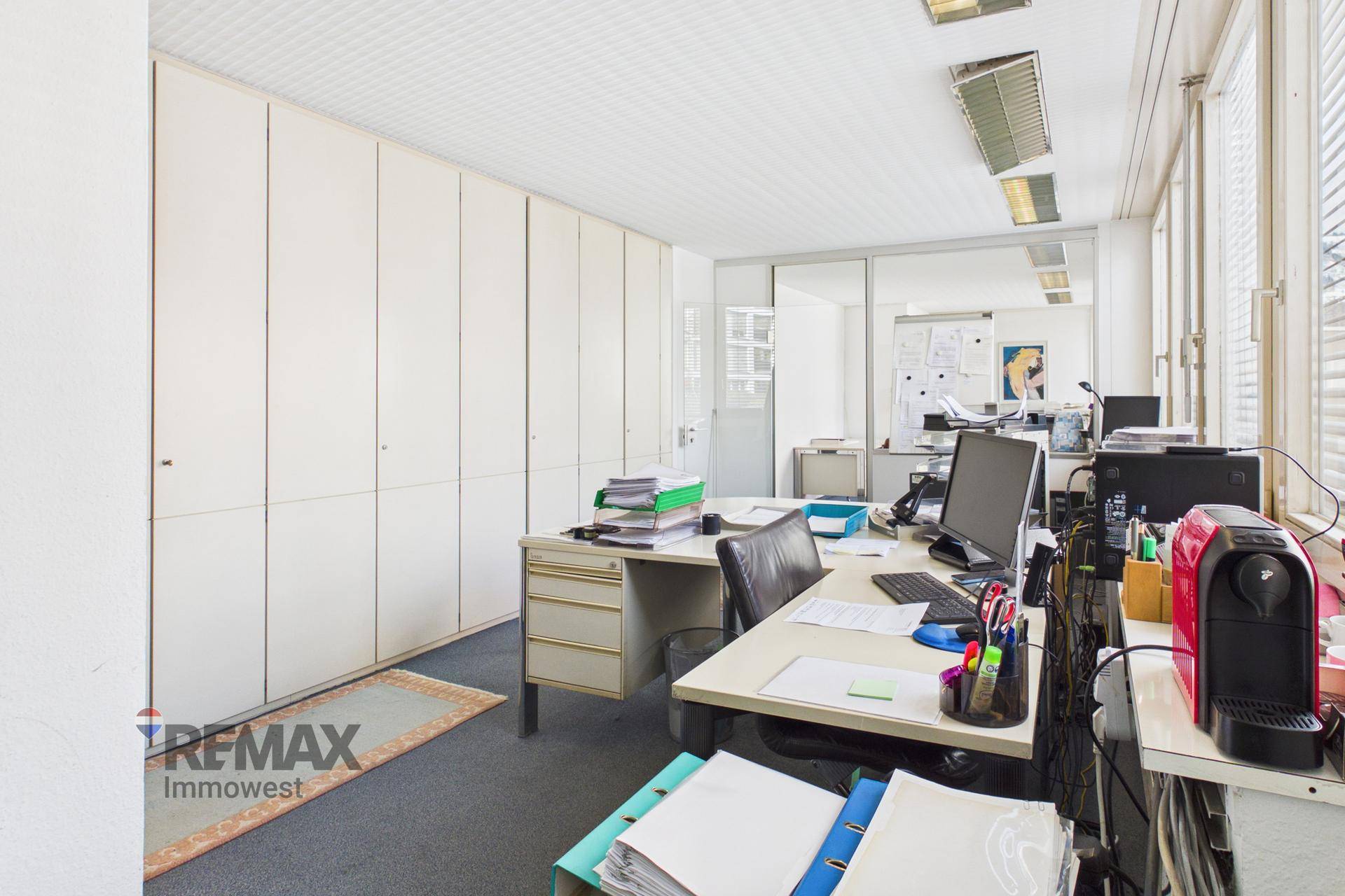 Büroarbeitsplatz mit weißen Einbauschränken, Schreibtisch mit Computer und Blick durch eine Glastrennwand.