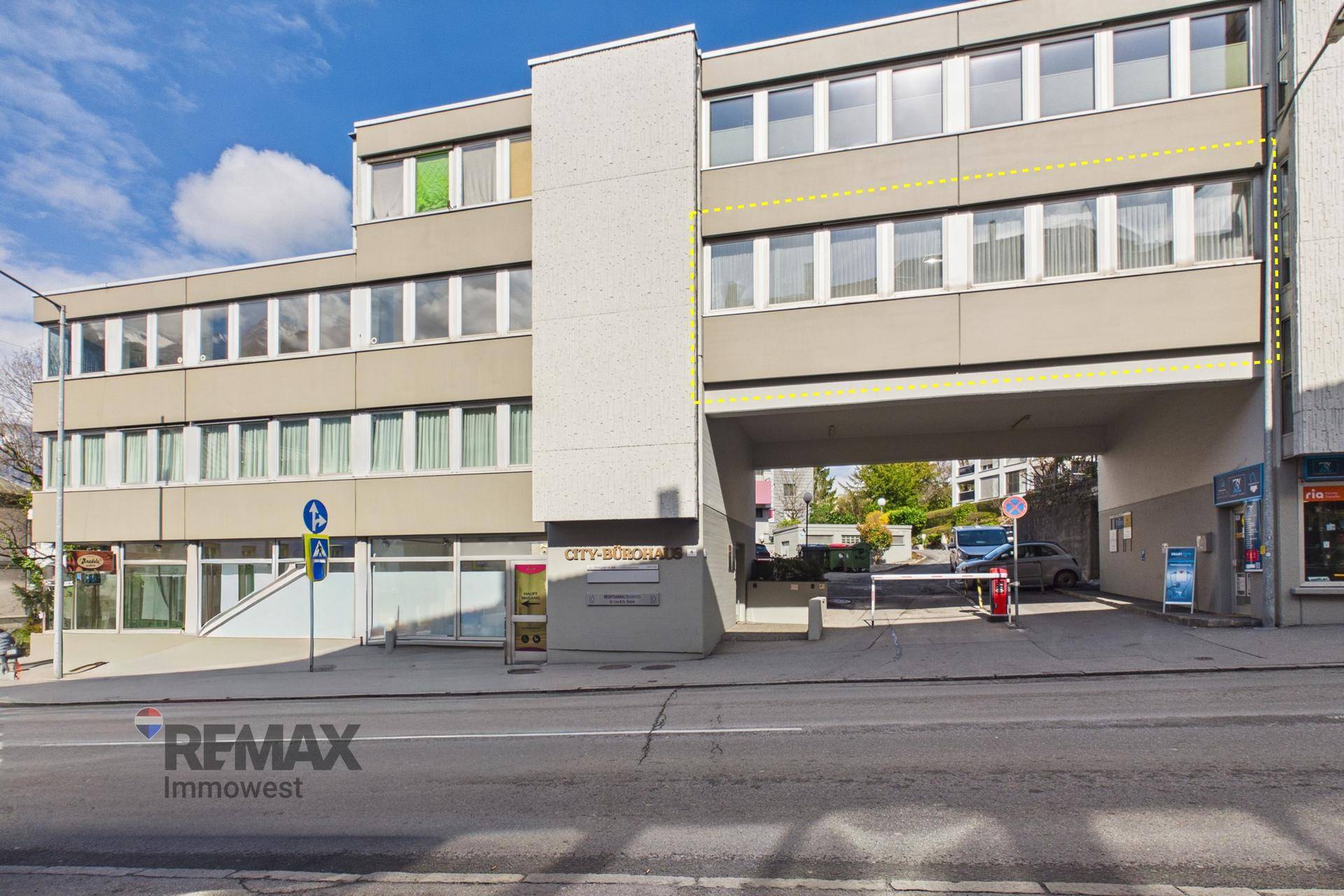 Außenansicht eines Geschäftsgebäudes von der Straße aus mit mehreren Etagen und einem Durchgang.