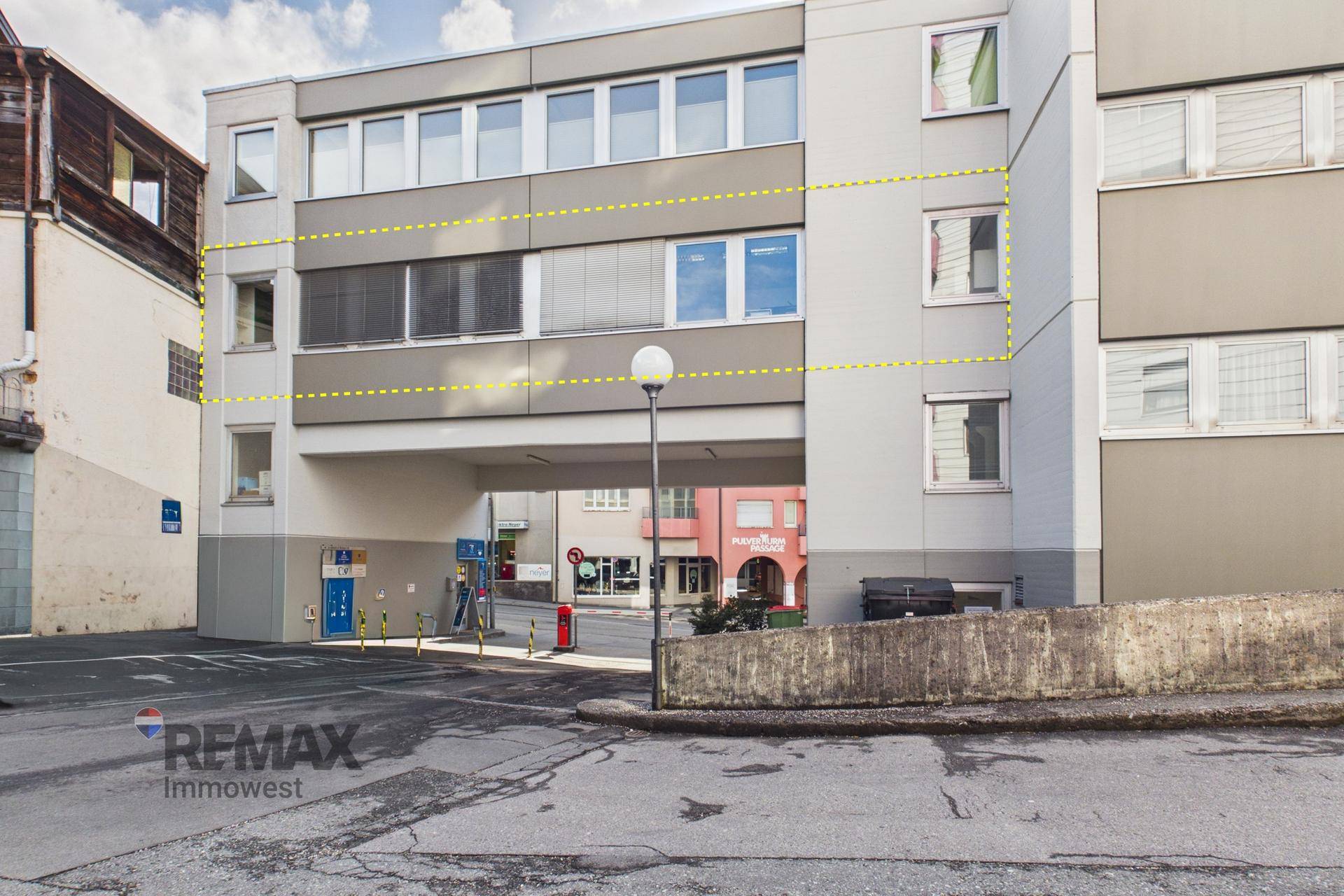 Seitenansicht des Geschäftsgebäudes mit einem Durchgang und einem Parkbereich im Vordergrund.