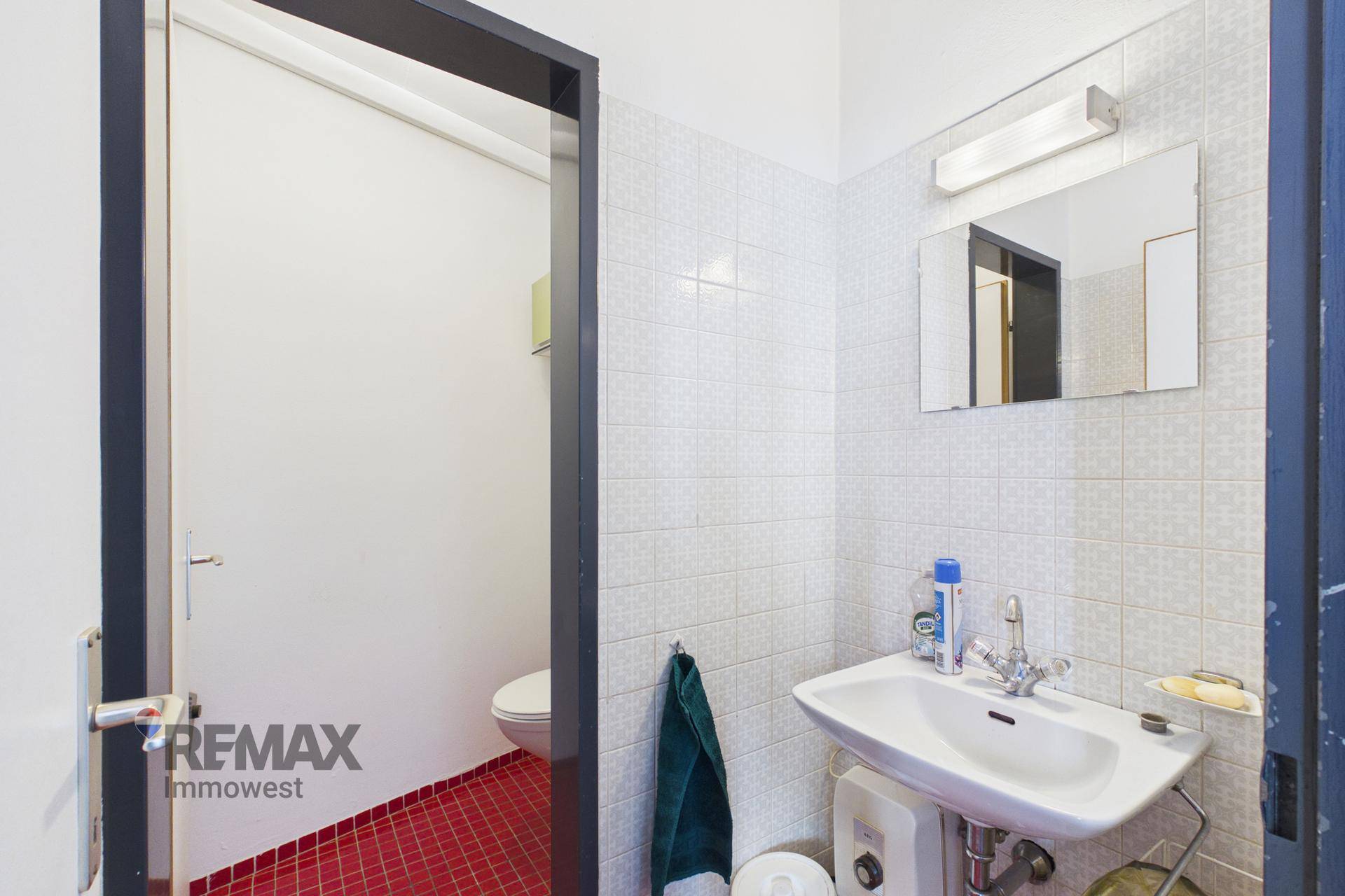 Kleines Gäste-WC mit Waschbecken, Spiegel und auffälligem roten Fliesenboden.