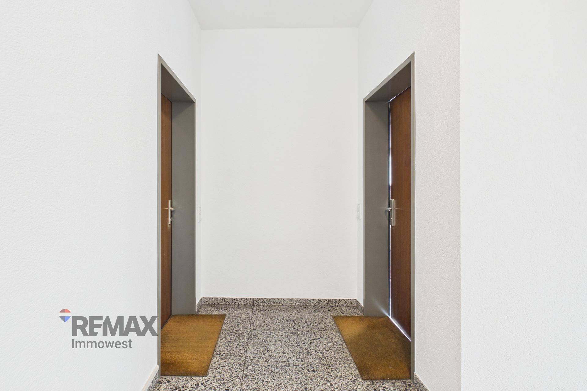 Heller Flur mit zwei Holztüren und einem gemusterten Terrazzo-Boden.