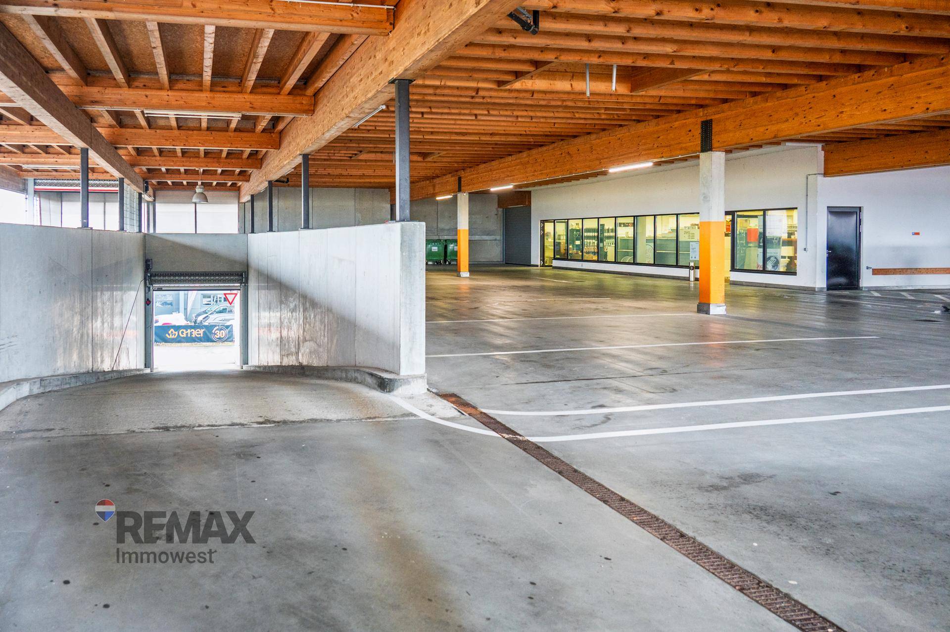 Überdachter Parkplatzbereich mit Betonboden und sichtbaren Holzdeckenbalken.