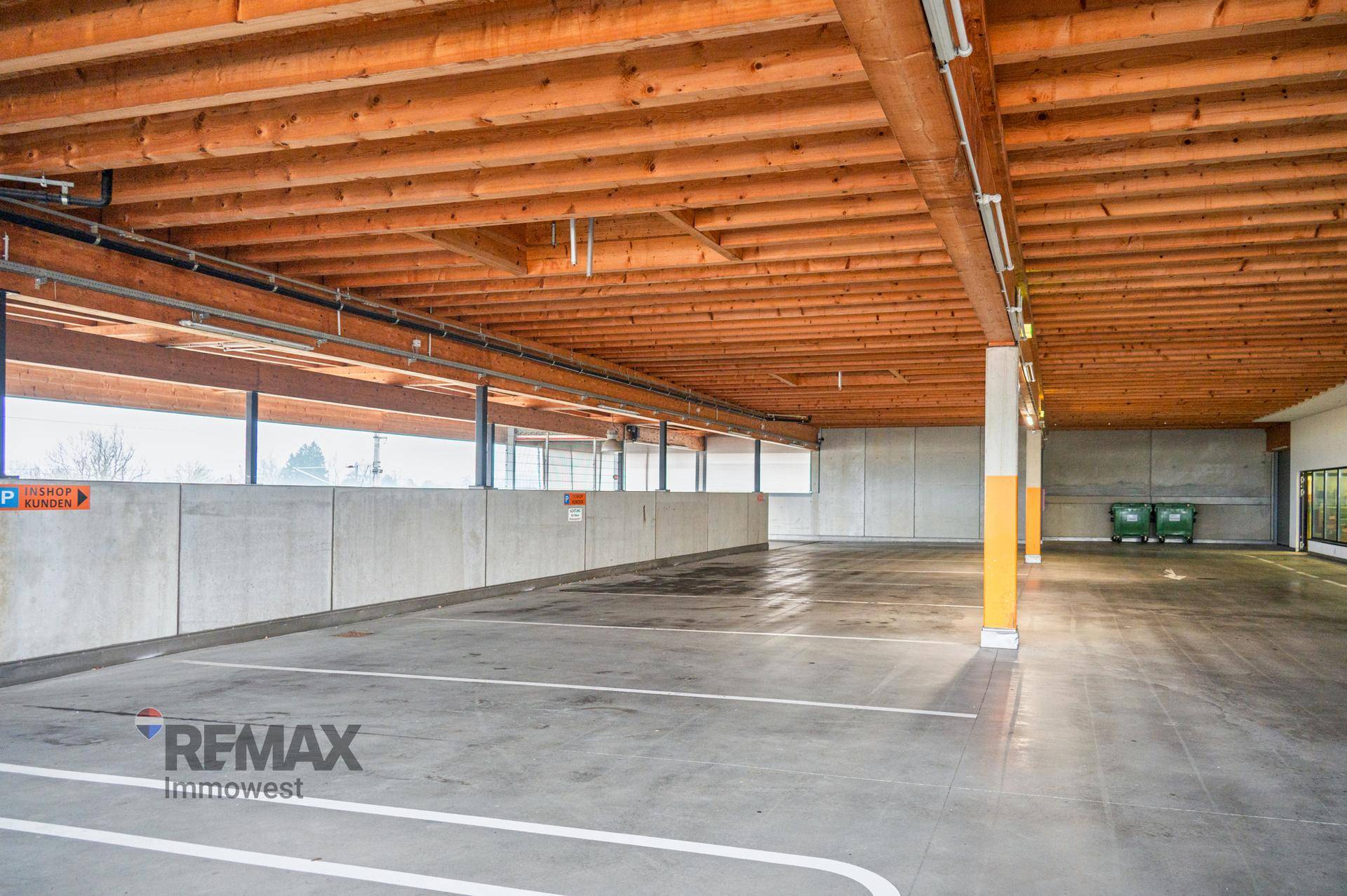 Heller überdachter Parkplatzbereich mit Betonwänden und Holzdeckenkonstruktion.
