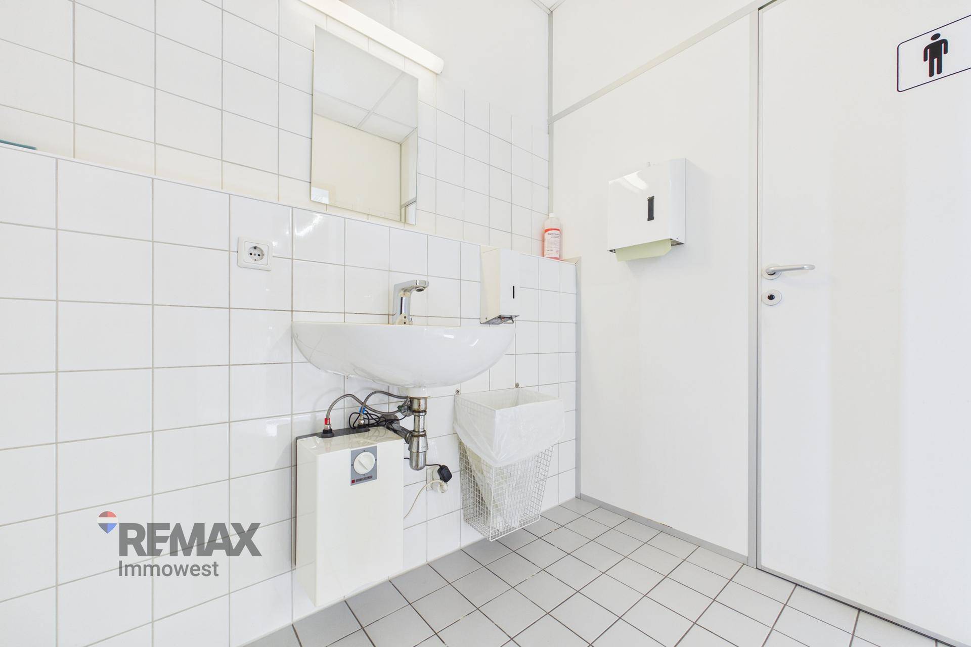 Saubere, geflieste Toilette mit Waschbecken, Spiegel und weißer Einrichtung.