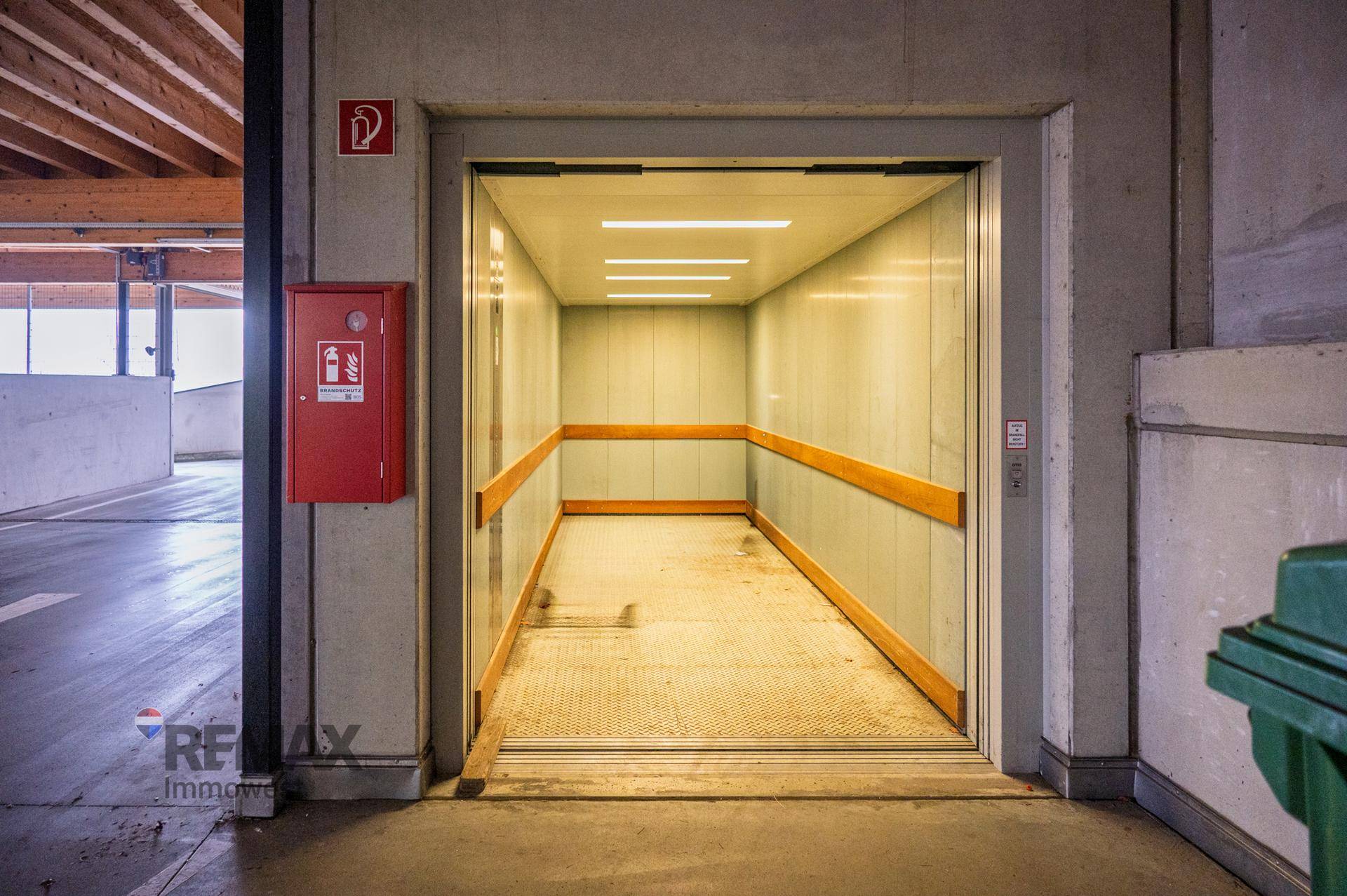 Geräumiger Lastenaufzug in einem Parkhaus mit robusten Wänden und sichtbarer Holzbalkendecke.