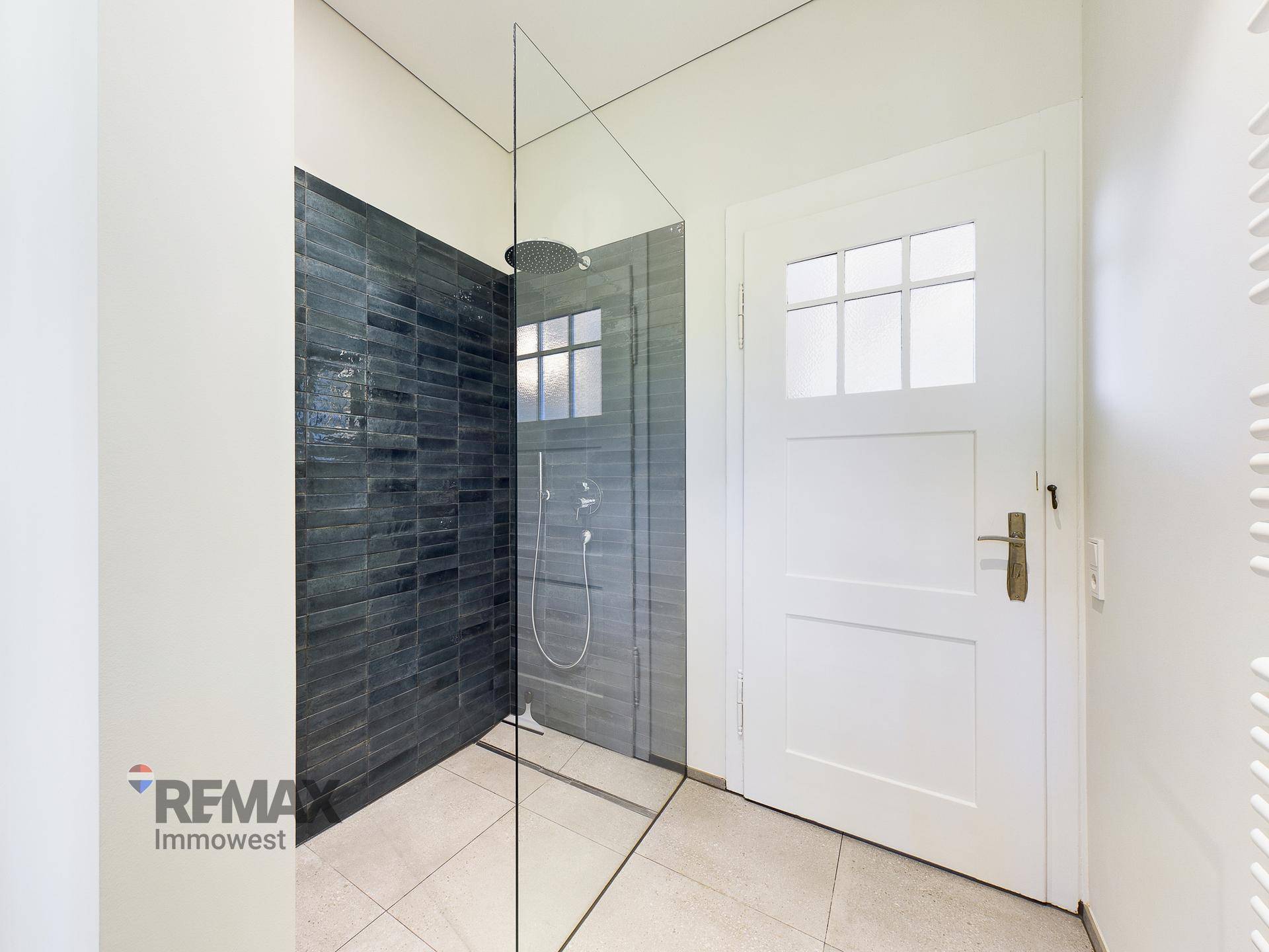 Modernes Badezimmer mit begehbarer Dusche, dunklen Fliesen und Glasabtrennung.