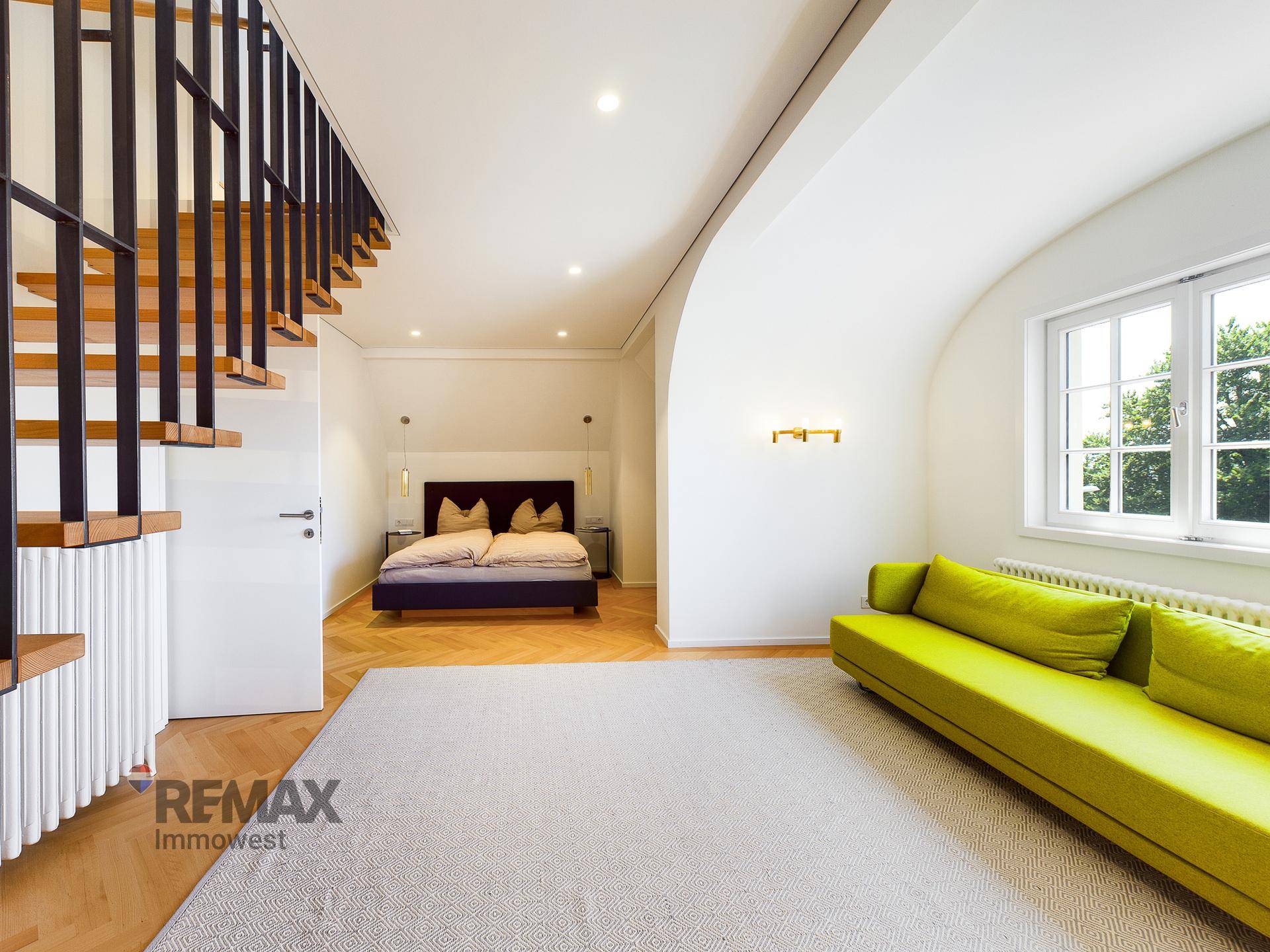 Heller Wohnbereich mit moderner Treppe, Parkettboden und einem Sofa in leuchtendem Grün.