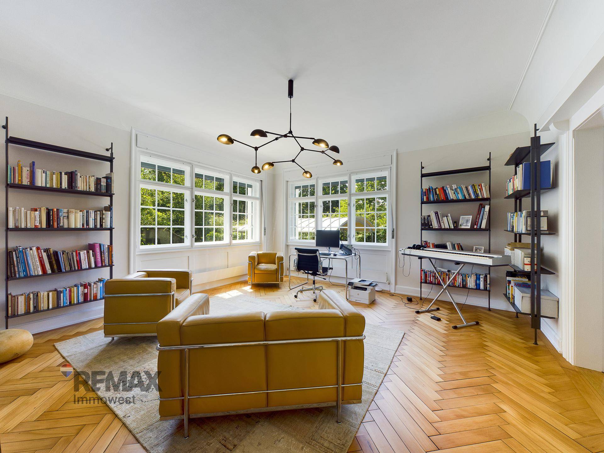 Geräumiges Arbeitszimmer mit Bücherregalen, gelben Ledersofas und Parkettboden.