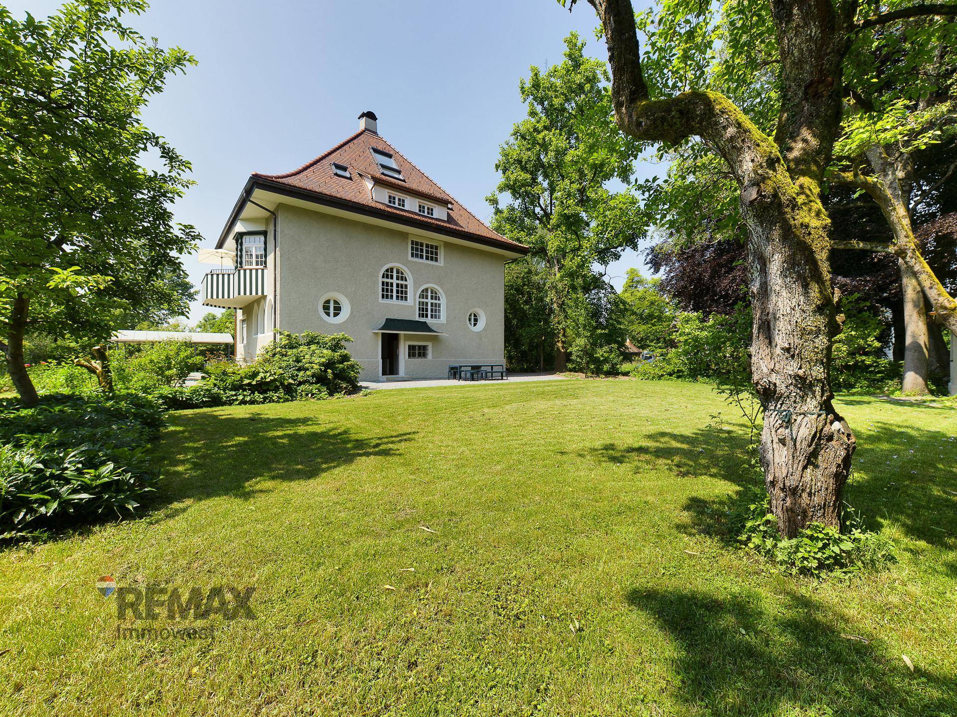 Historische Villa mit gepflegtem Garten, großen Fenstern und Balkon.