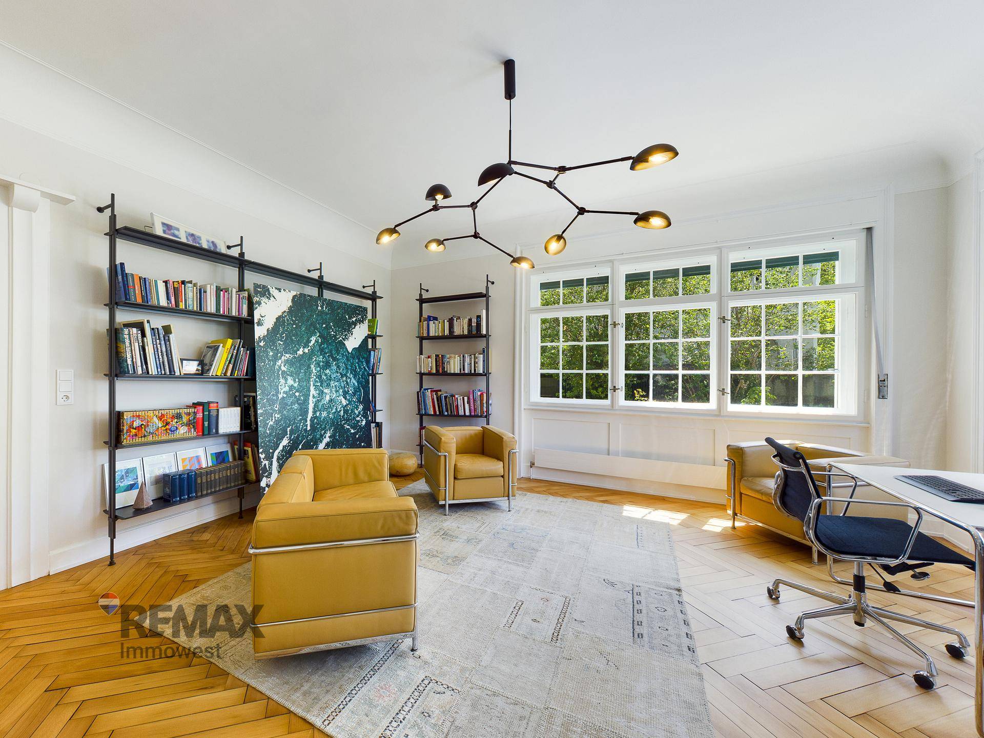 Helles Arbeitszimmer mit Bücherregalen, gelben Ledermöbeln und großen Fenstern.