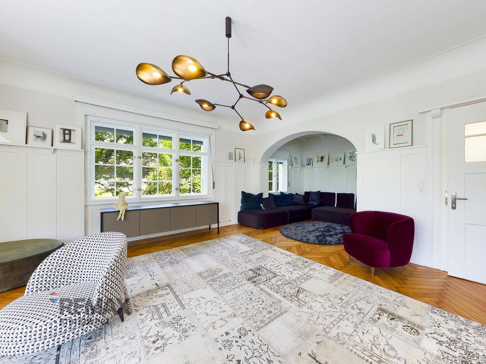 Stilvolles Wohnzimmer mit Parkettboden, modernen Möbeln und großen Fenstern.