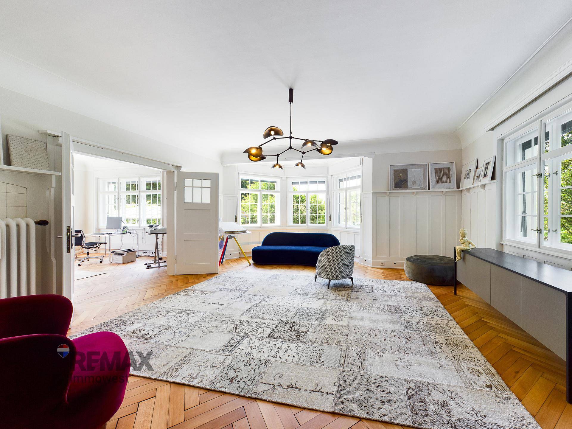 Großzügiges Wohnzimmer mit Parkettboden, eleganten Möbeln und viel Tageslicht.