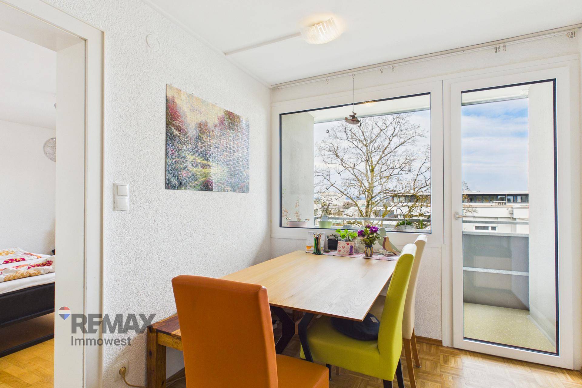 Gemütlicher Essbereich mit Holztisch, bunten Stühlen und Balkonzugang.