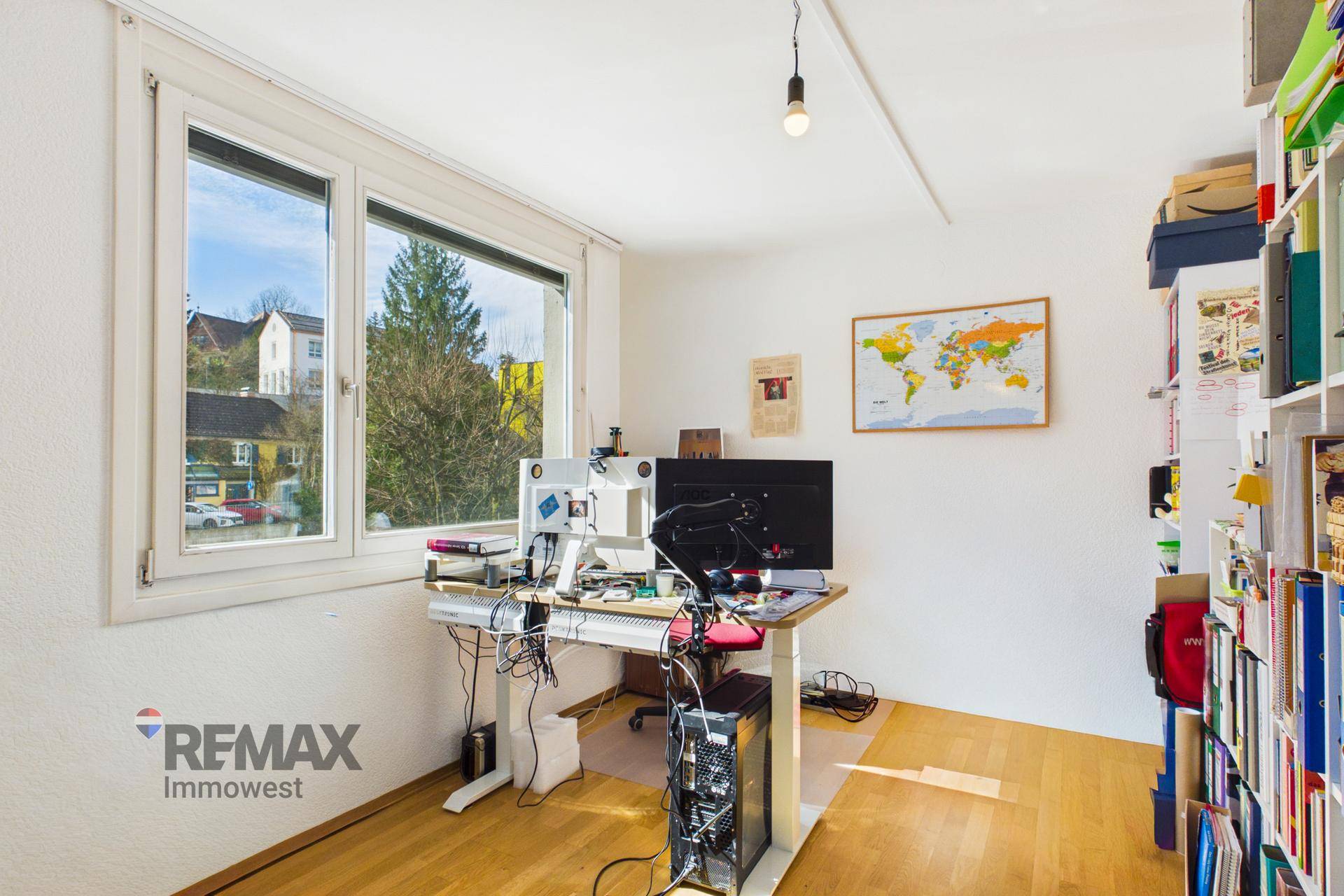 Helles Arbeitszimmer mit Parkettboden, großem Fenster und Schreibtisch mit Computern.
