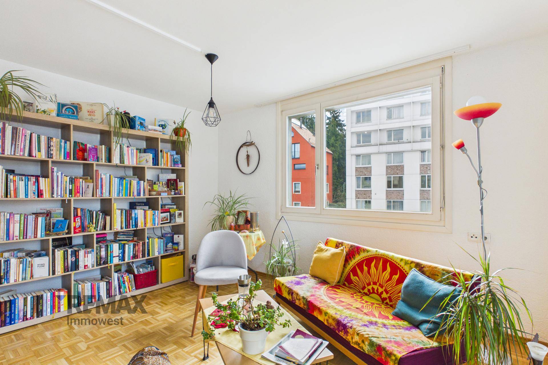Helles Wohnzimmer mit großem Bücherregal, Parkettboden und farbenfrohem Sofa.