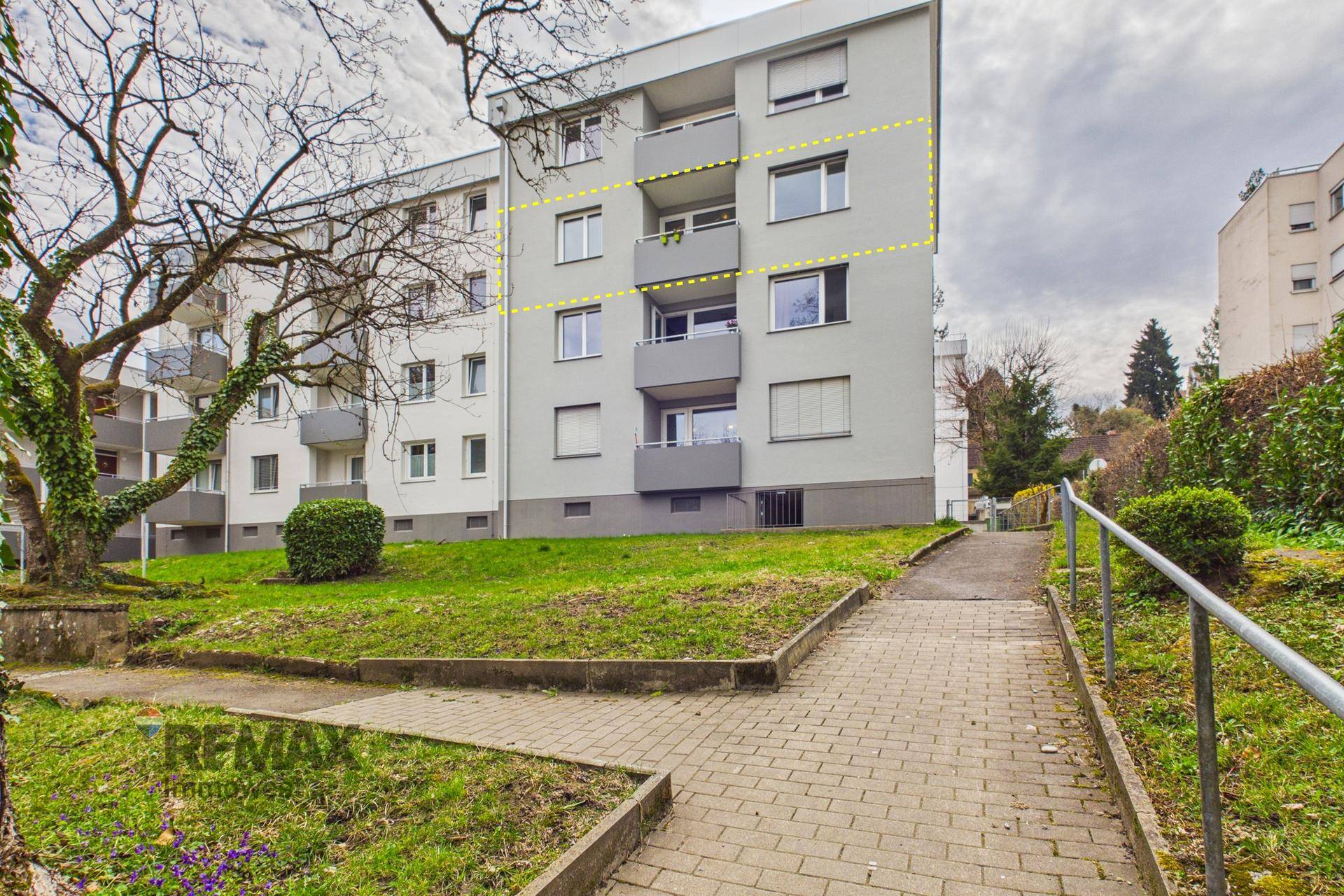 Mehrfamilienhaus mit Balkonen und Grünflächen im Vordergrund.