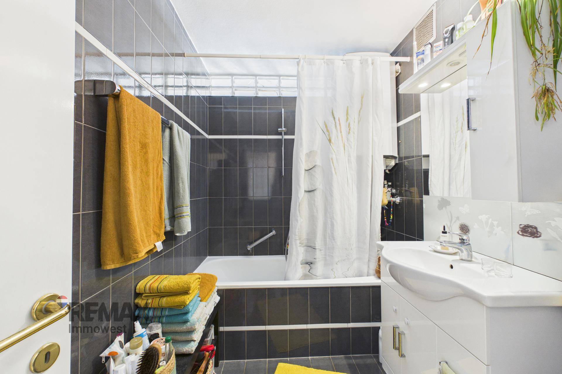 Badezimmer mit Badewanne, dunklen Fliesen und Waschbecken mit Spiegelschrank.