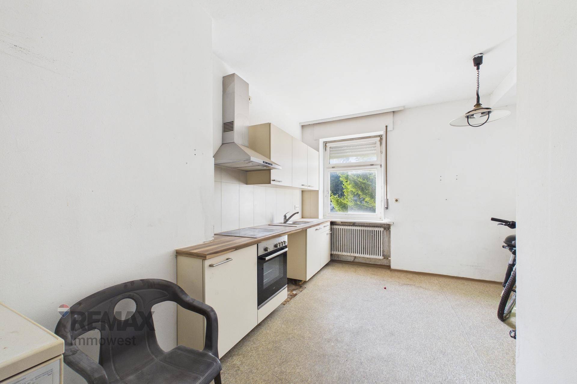 Kleine Küche mit beigen Schränken, Dunstabzugshaube und Fensterblick ins Grüne.