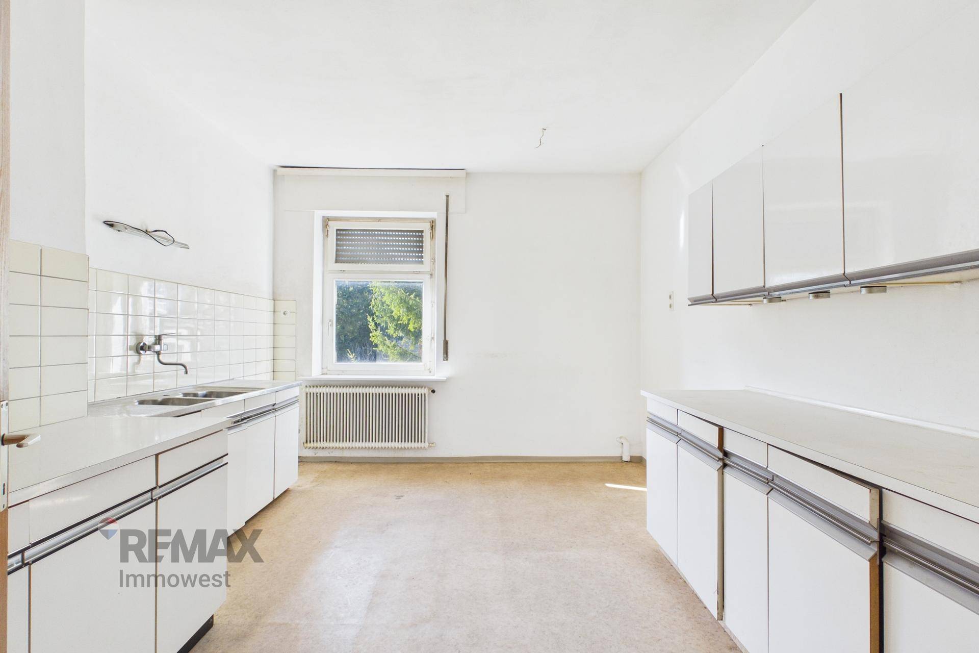 Leere Küche mit weißen Schränken, Spüle und einem Fenster.