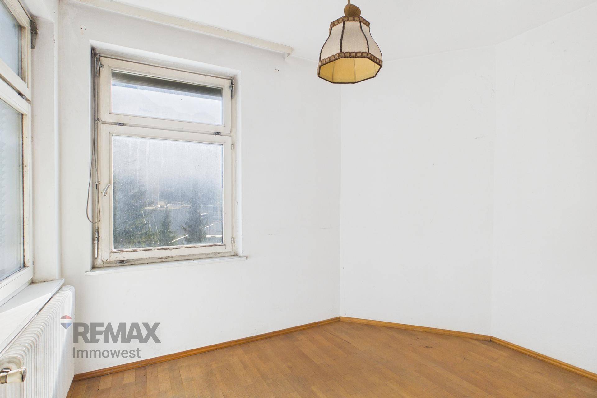 Helles Zimmer mit Fischgrätparkettboden und einem Fenster mit Blick nach draußen.