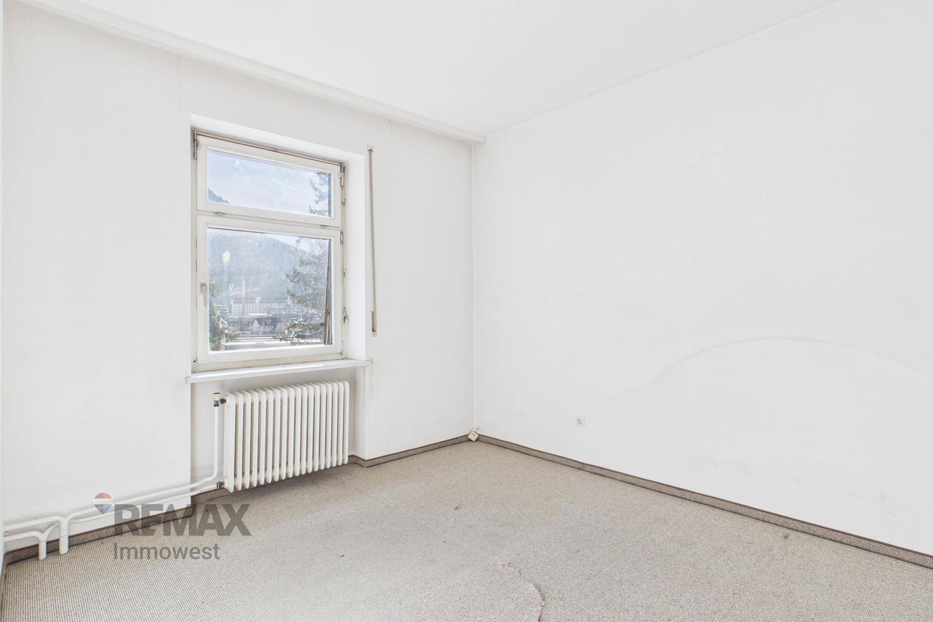 Leeres Zimmer mit Teppichboden und einem Fenster, das Tageslicht hereinlässt.