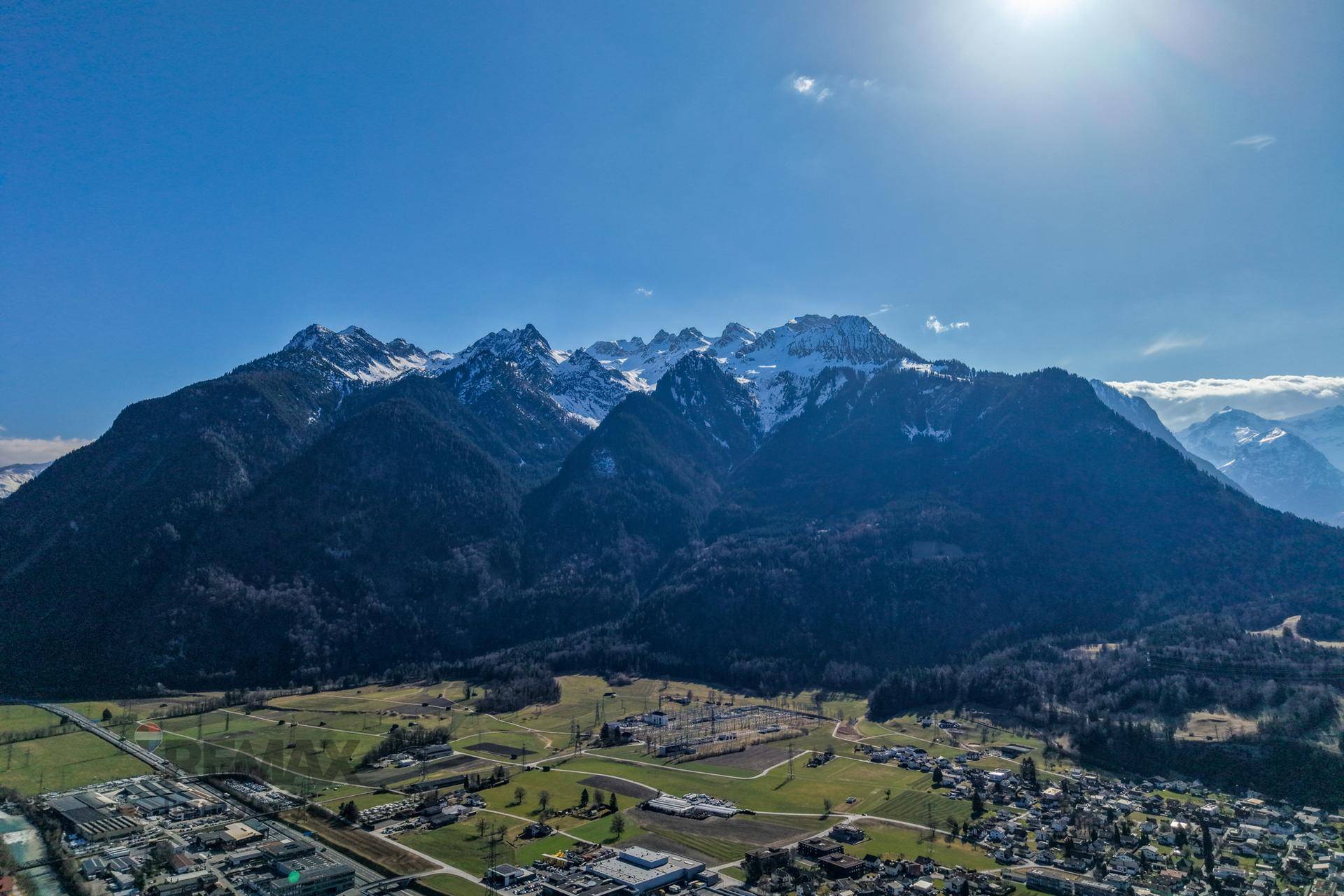 Majestätisches Bergpanorama mit schneebedeckten Gipfeln und weiten grünen Tälern unter blauem Himmel.