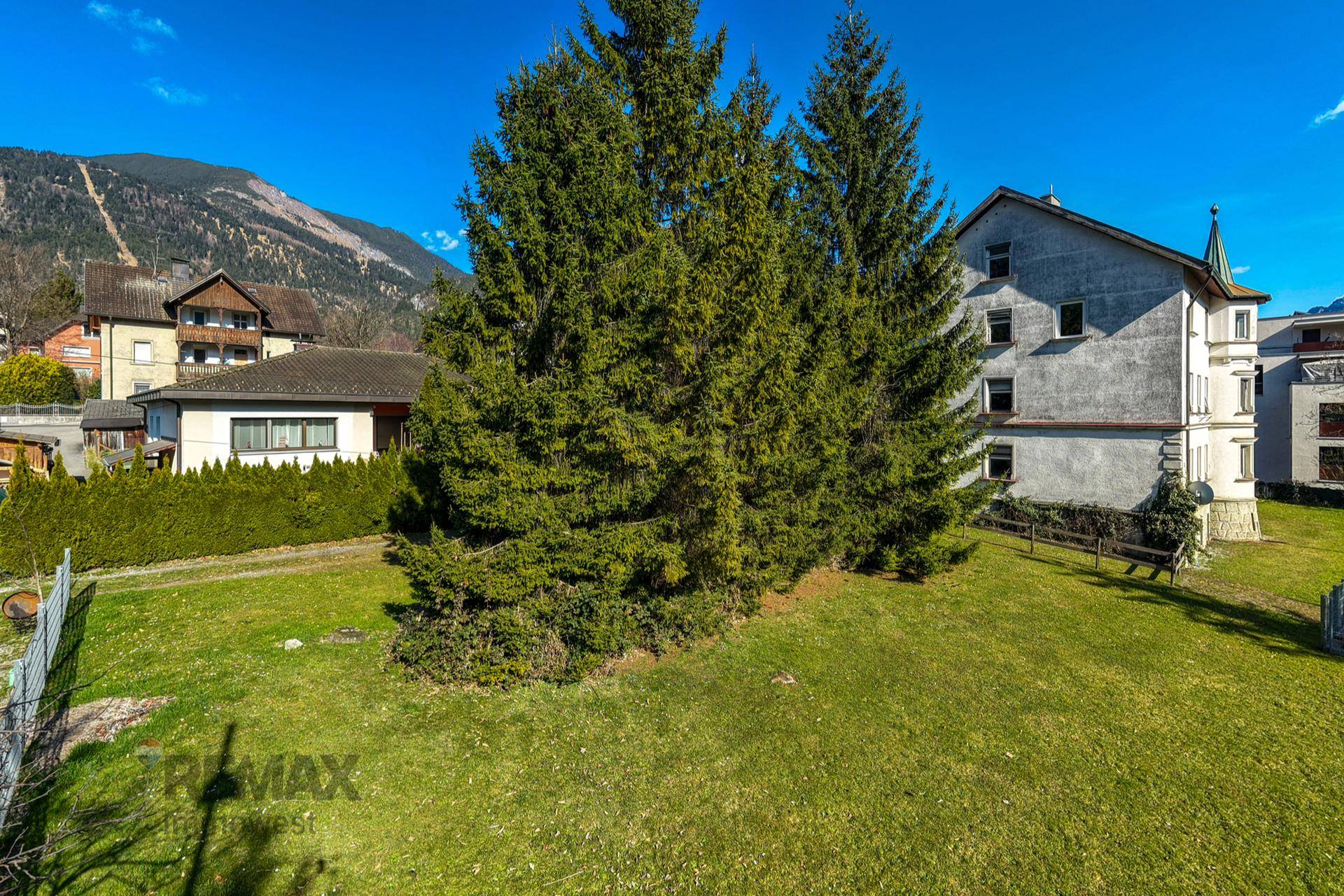 Großer Gartenbereich mit hohen Nadelbäumen und Blick auf das historische Gebäude.
