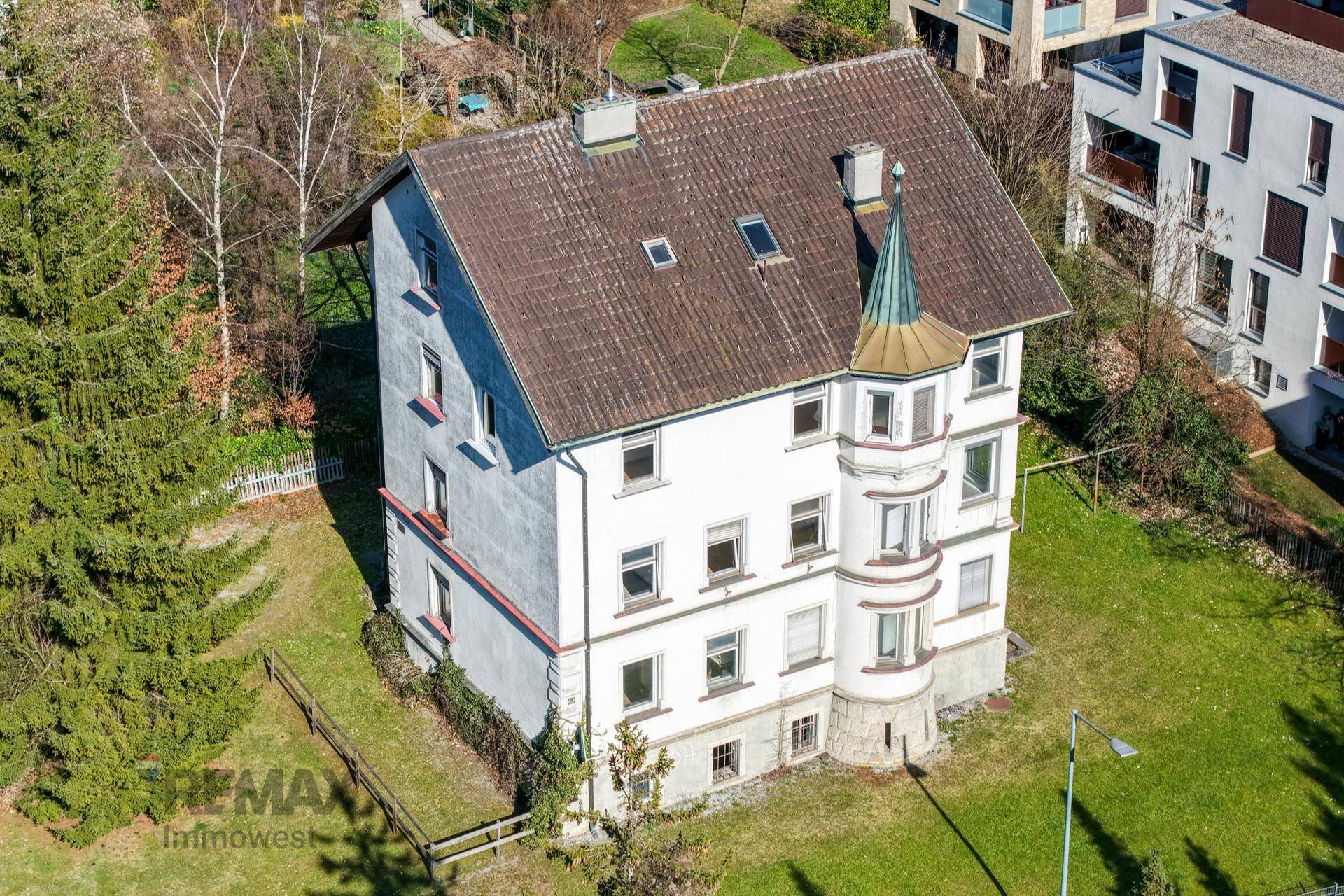 Luftaufnahme des historischen Gebäudes mit markantem Dach und umliegendem Grundstück.