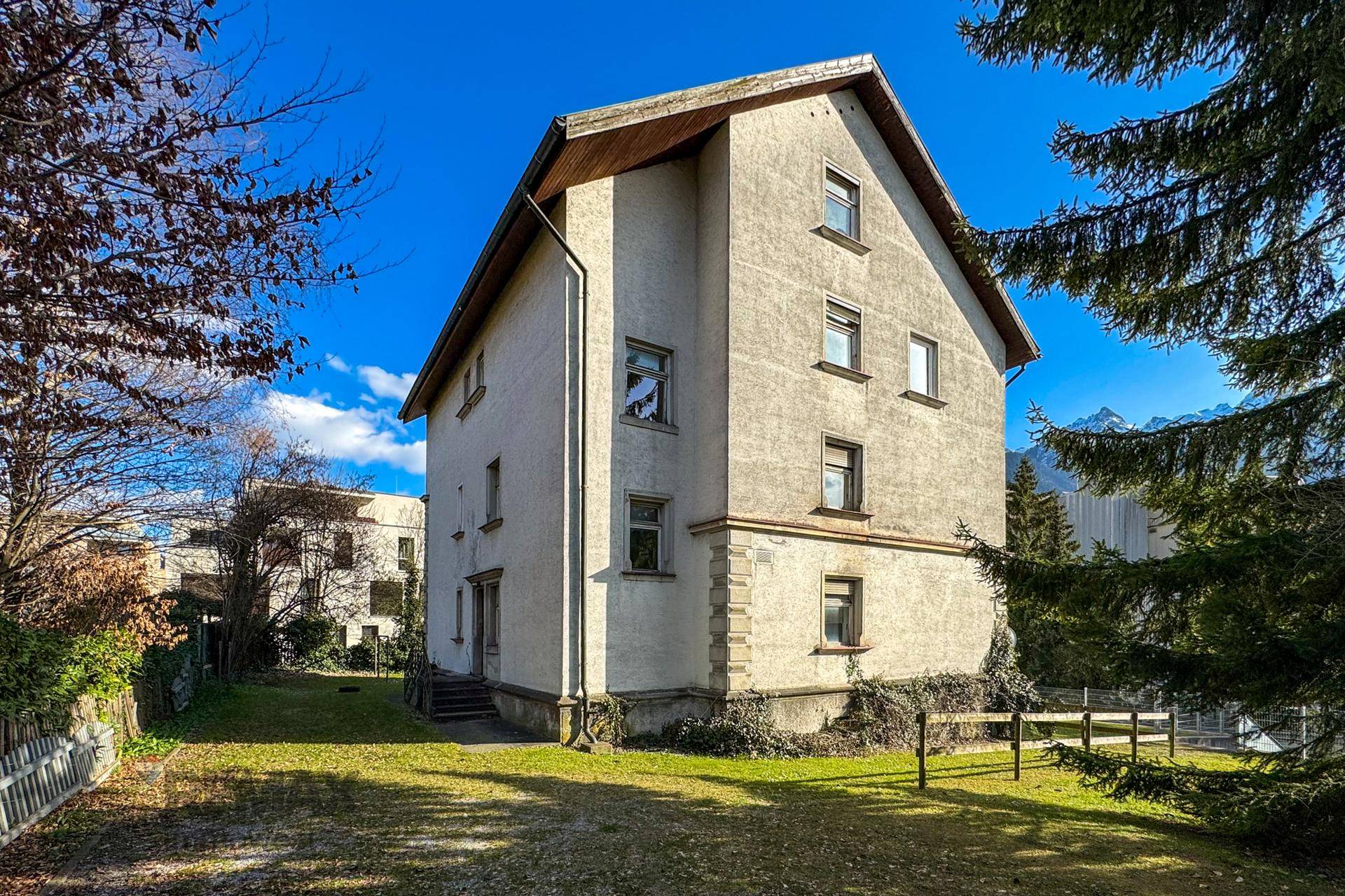 Ansicht des Mehrfamilienhauses von der Seite mit Gartenbereich und Blick auf die Berge.