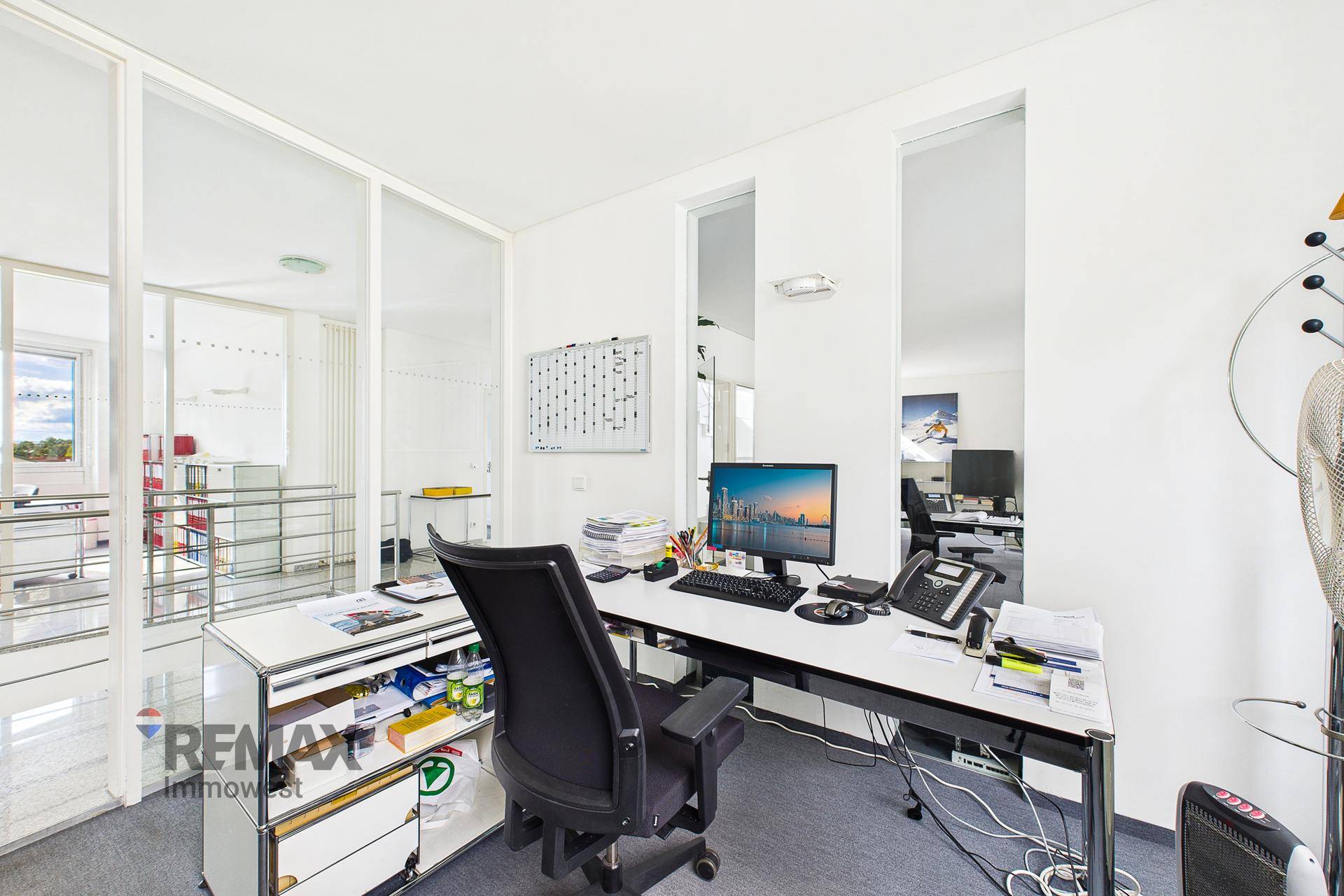 Moderner Bürobereich mit Glaswänden und Blick auf den Flur, ausgestattet mit Schreibtischen und Bürostühlen.