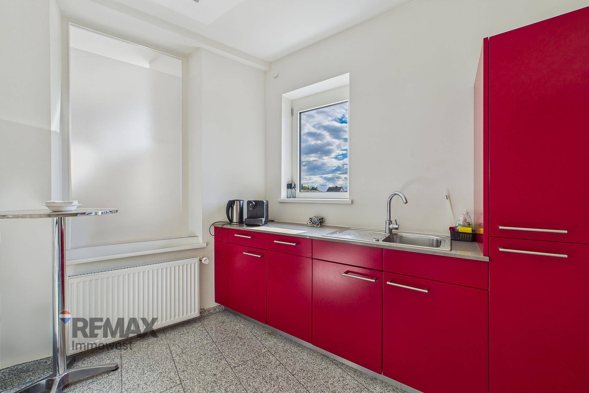 Funktionale Küchenzeile mit roten Unterschränken, Spüle und Fenster, ausgestattet für den täglichen Gebrauch.