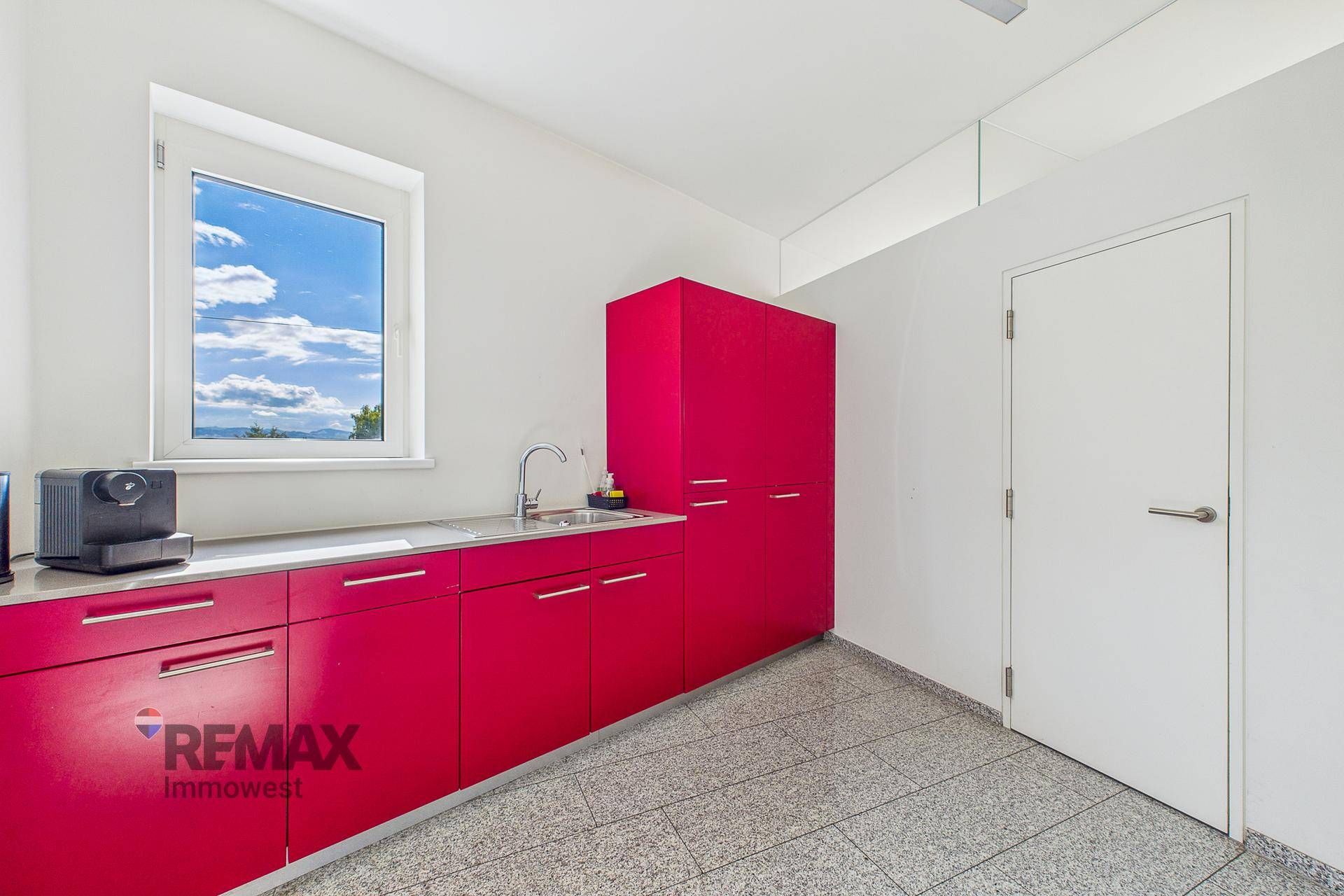 Moderne Küchenzeile mit leuchtend roten Schränken, Spüle und Fenster, ideal für Pausen.