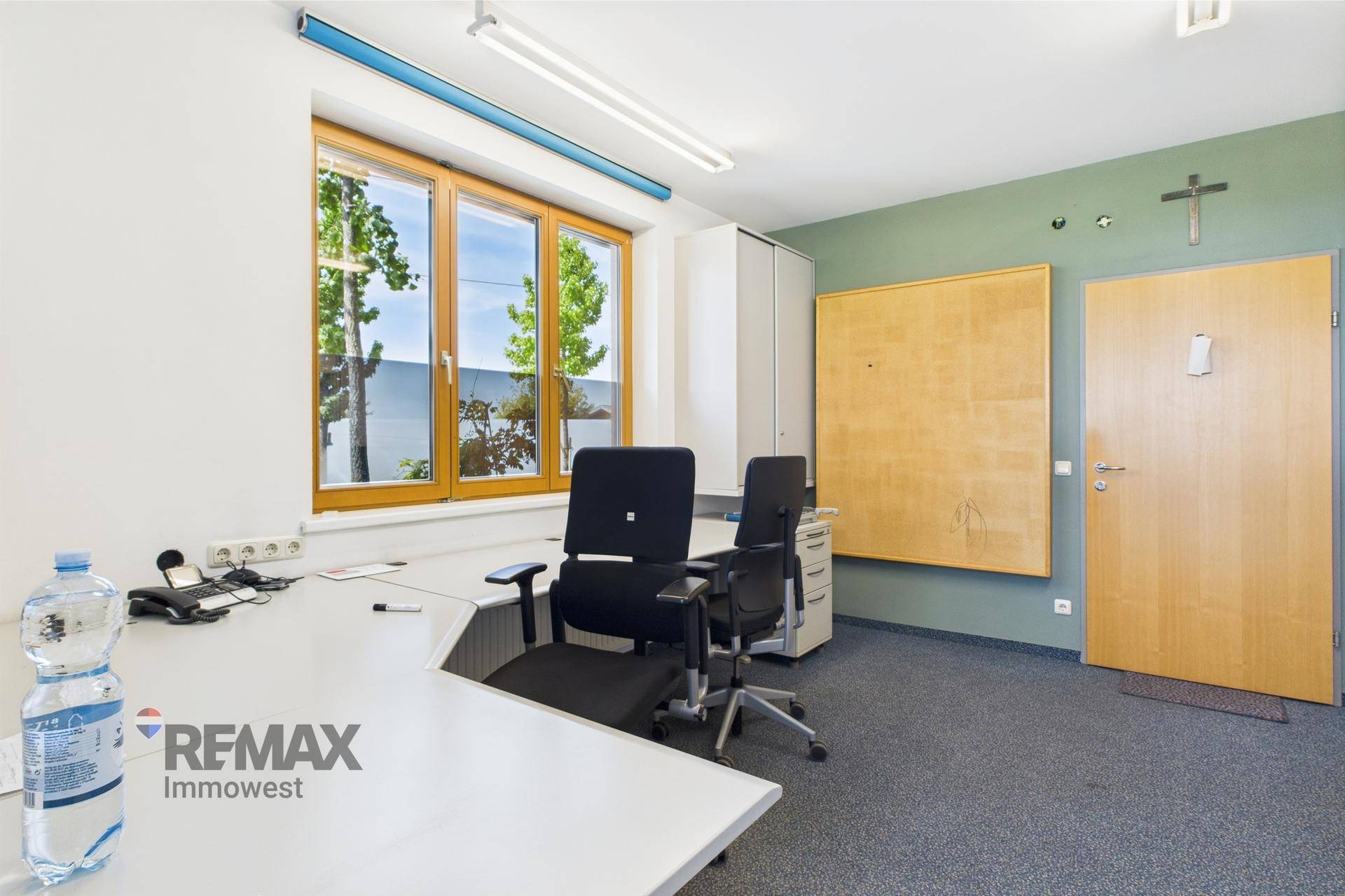 Helles Büro mit zwei Arbeitsplätzen, Teppichboden und einem Fenster mit Blick nach draußen.