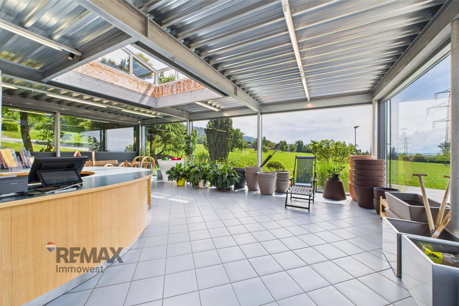 Heller Verkaufsraum mit großen Glasfronten, Fliesenboden und Blick auf die umliegende Landschaft.