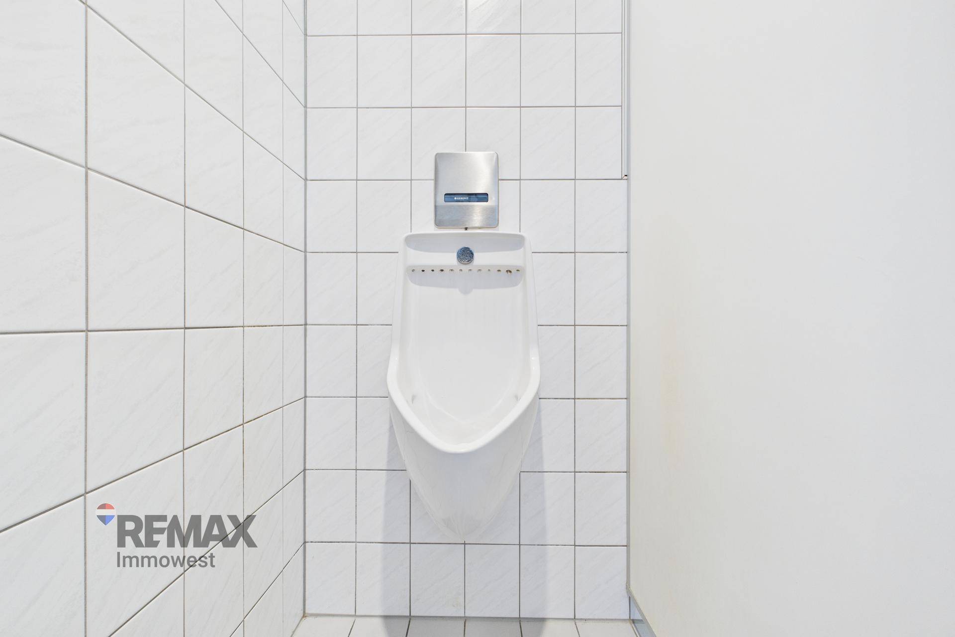 Sauberes WC mit Urinal und weißen Fliesen an den Wänden.