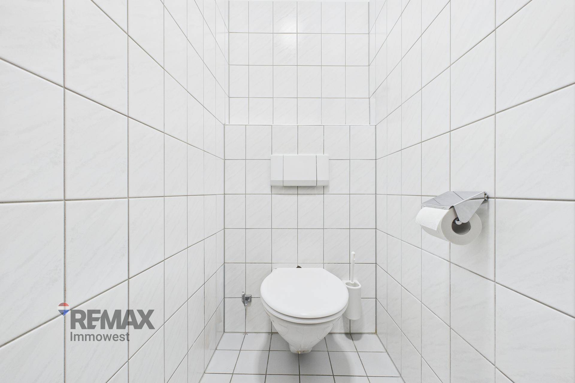 Toilettenkabine mit Wand-WC und weißen Fliesen an Wänden und Boden.