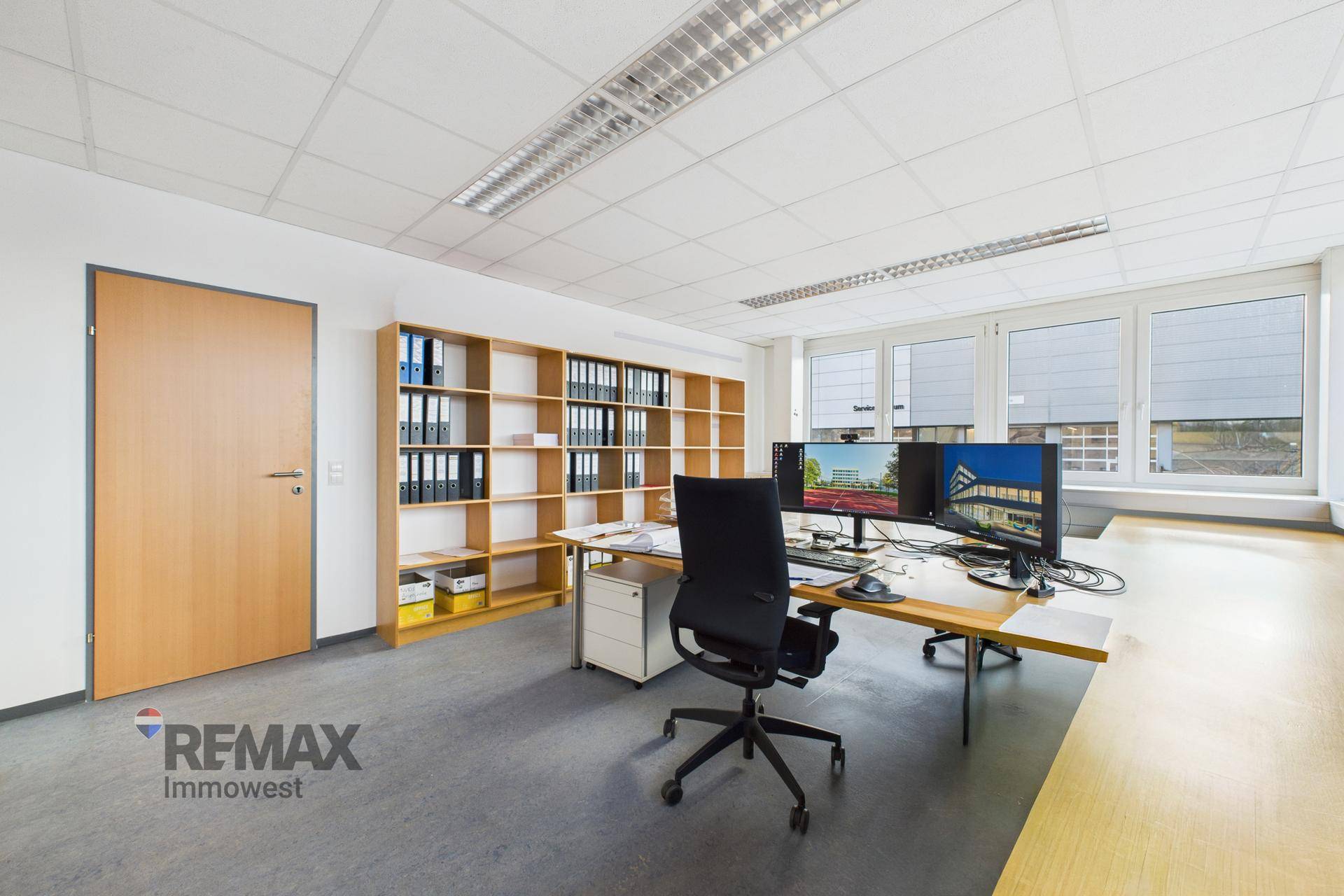 Modernes Büro mit Holzregalen, Schreibtisch und viel Tageslicht durch große Fenster.