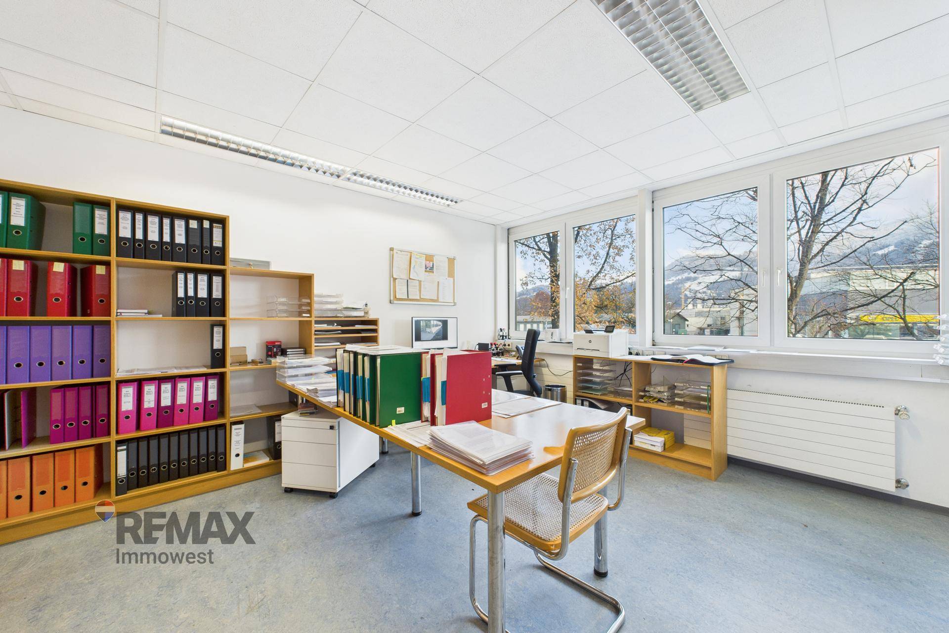 Helles Büro mit Holzregalen, Schreibtisch und Blick auf die Berge durch die Fenster.