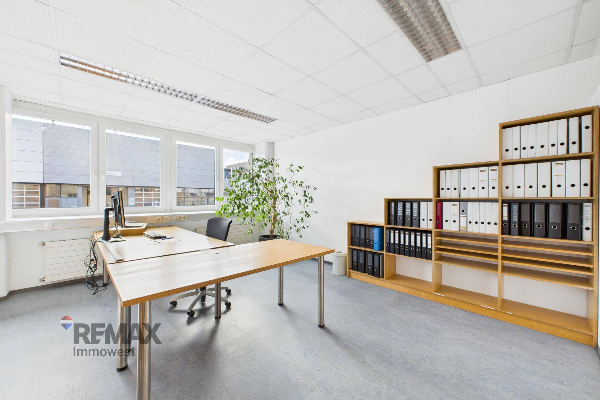 Modernes Büro mit Schreibtischen, Regalen und Blick auf die Umgebung durch die Fenster.