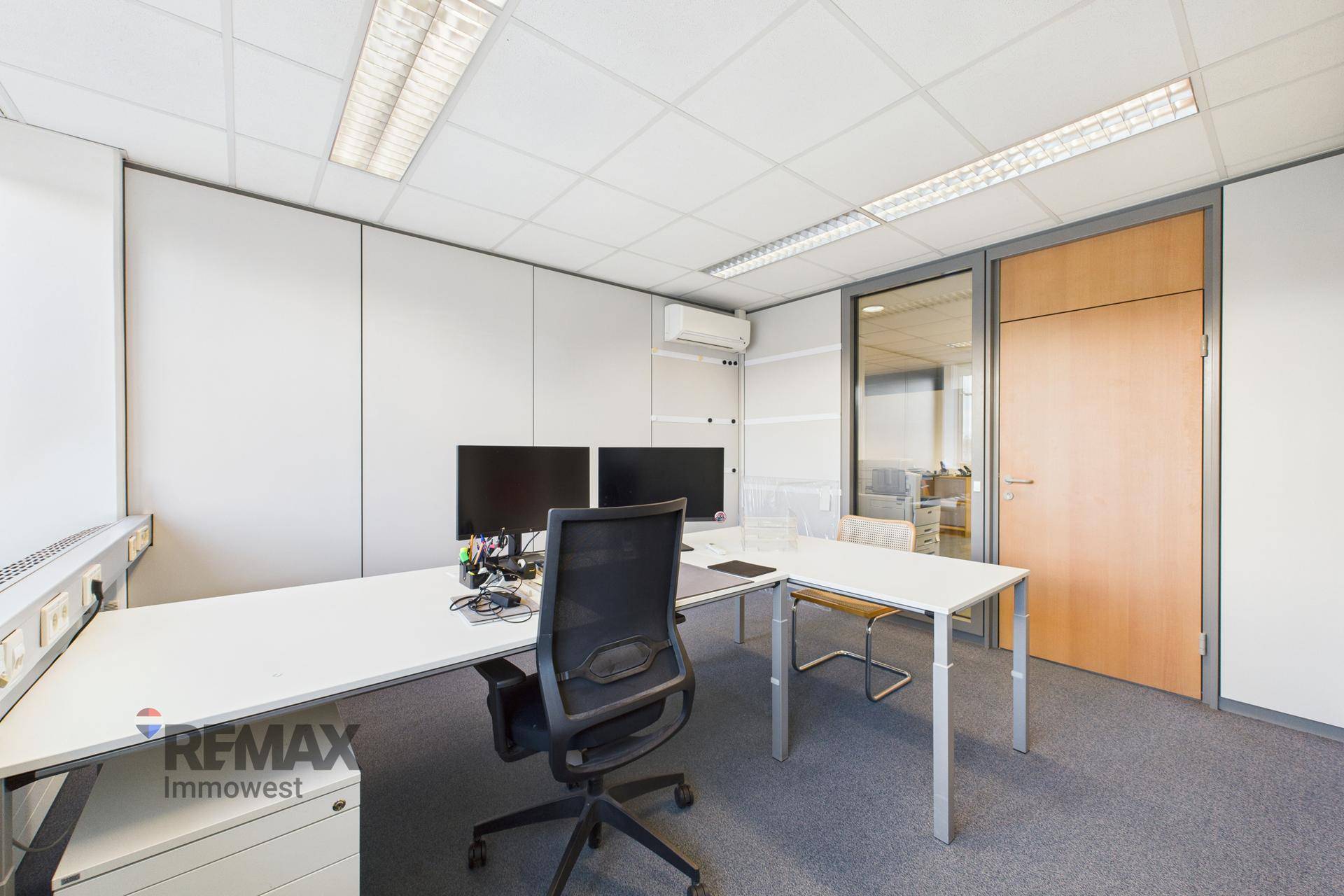 Büro mit Schreibtisch, Bürostuhl und einer Glaswand, die den Raum abtrennt.