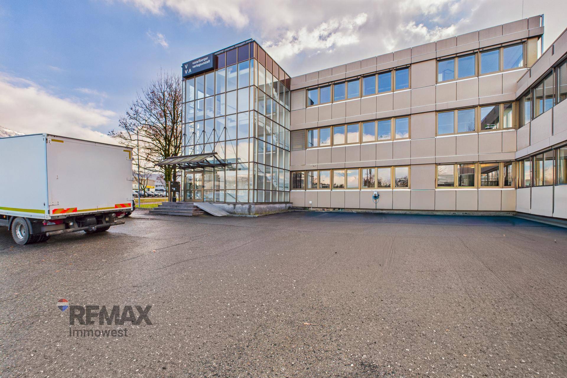 Bürogebäude mit großem gepflasterten Bereich und einem Lieferwagen davor.