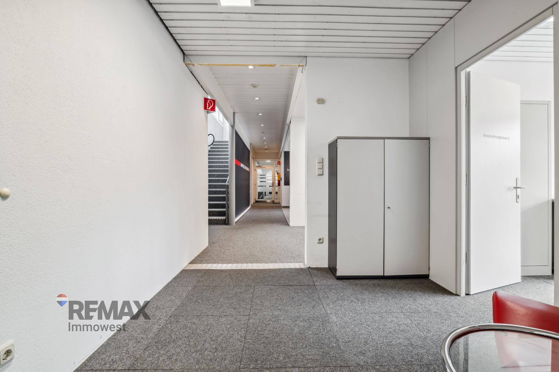 Langer Flur mit Teppichboden und Zugang zu verschiedenen Büros sowie einer Treppe.