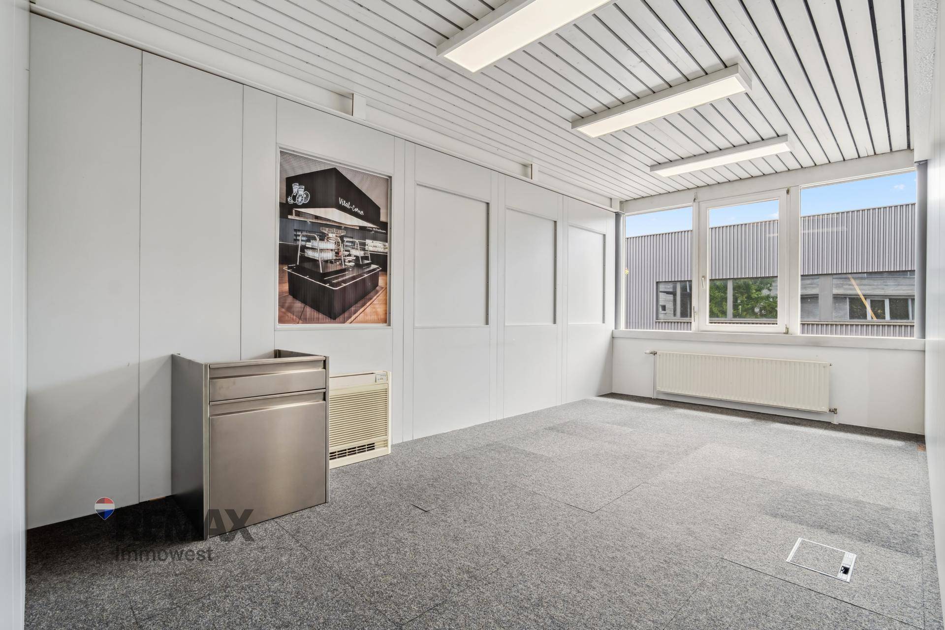 Leeres Büro mit Teppichboden, Heizkörper und großen Fenstern, bereit zur individuellen Gestaltung.
