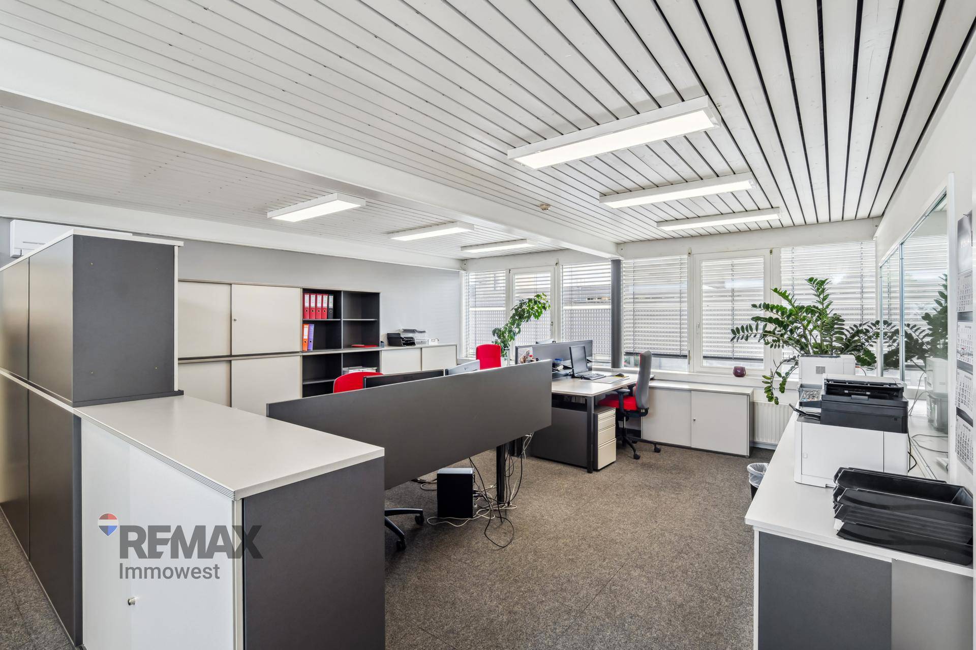 Modern eingerichtetes Büro mit mehreren Arbeitsplätzen, Stauraum und viel Tageslicht durch große Fenster.