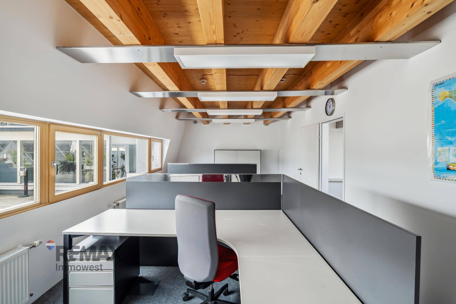 Helles Büro mit Holzbalkendecke, Teppichboden und modernen Arbeitsplätzen, ideal für konzentriertes Arbeiten.