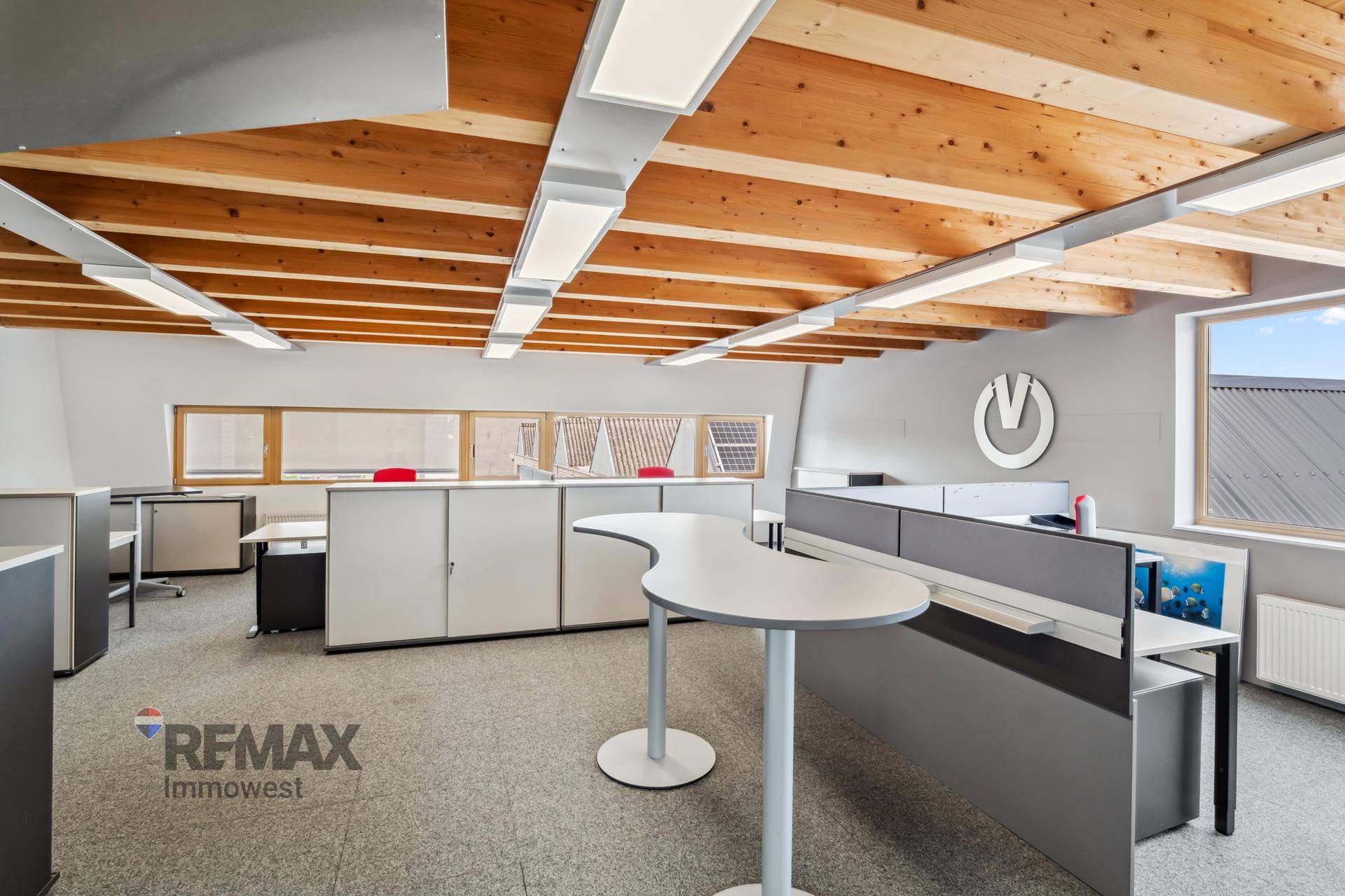 Modernes Büro mit Holzbalkendecke, Teppichboden und mehreren Arbeitsplätzen unter dem Dach.